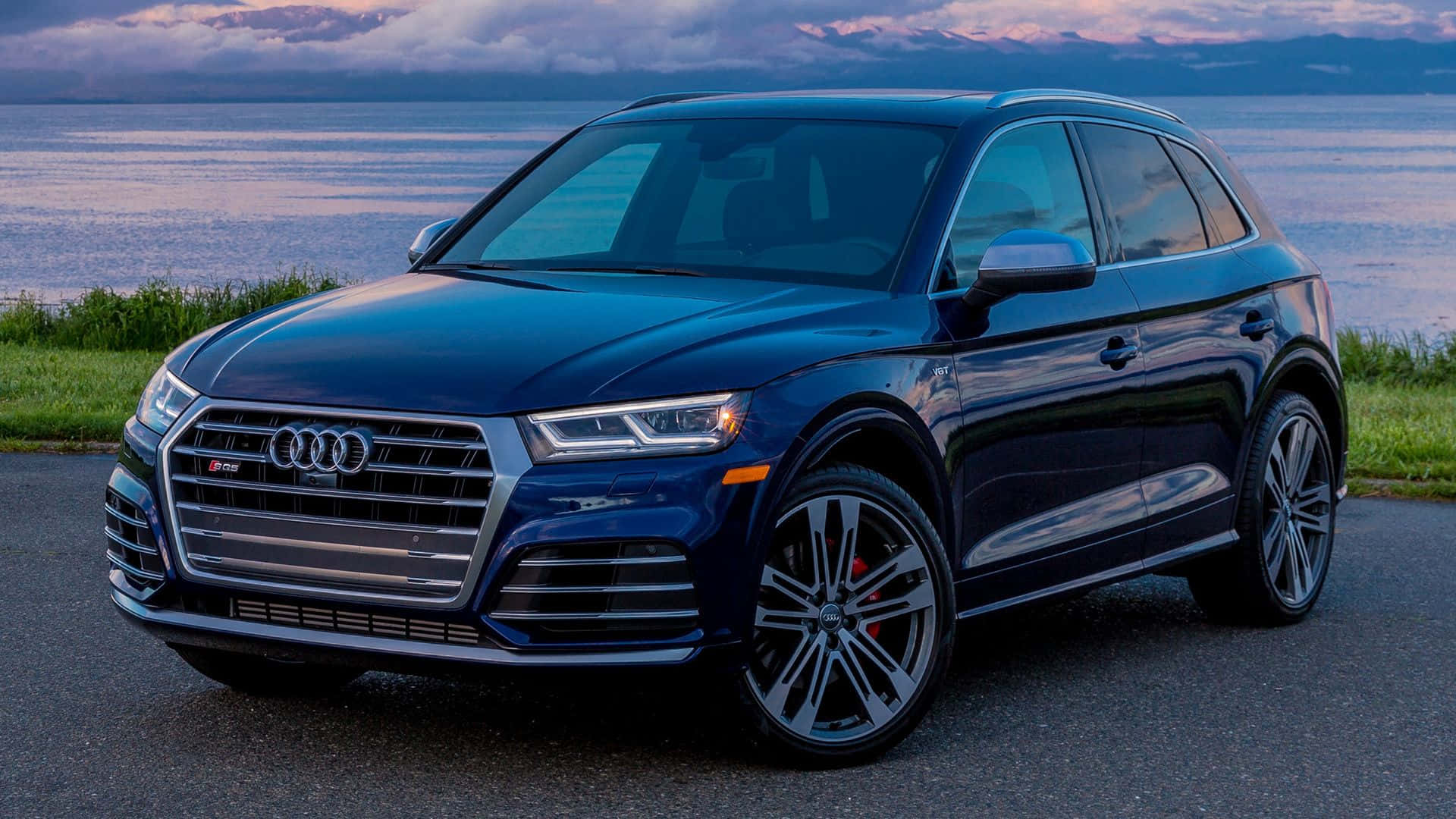 Audi Sq5 桌布 壁紙 — 一架時尚深藍色 Audi SQ5 SUV 停泊在黃昏時分寧靜的湖邊，背景有山巒。