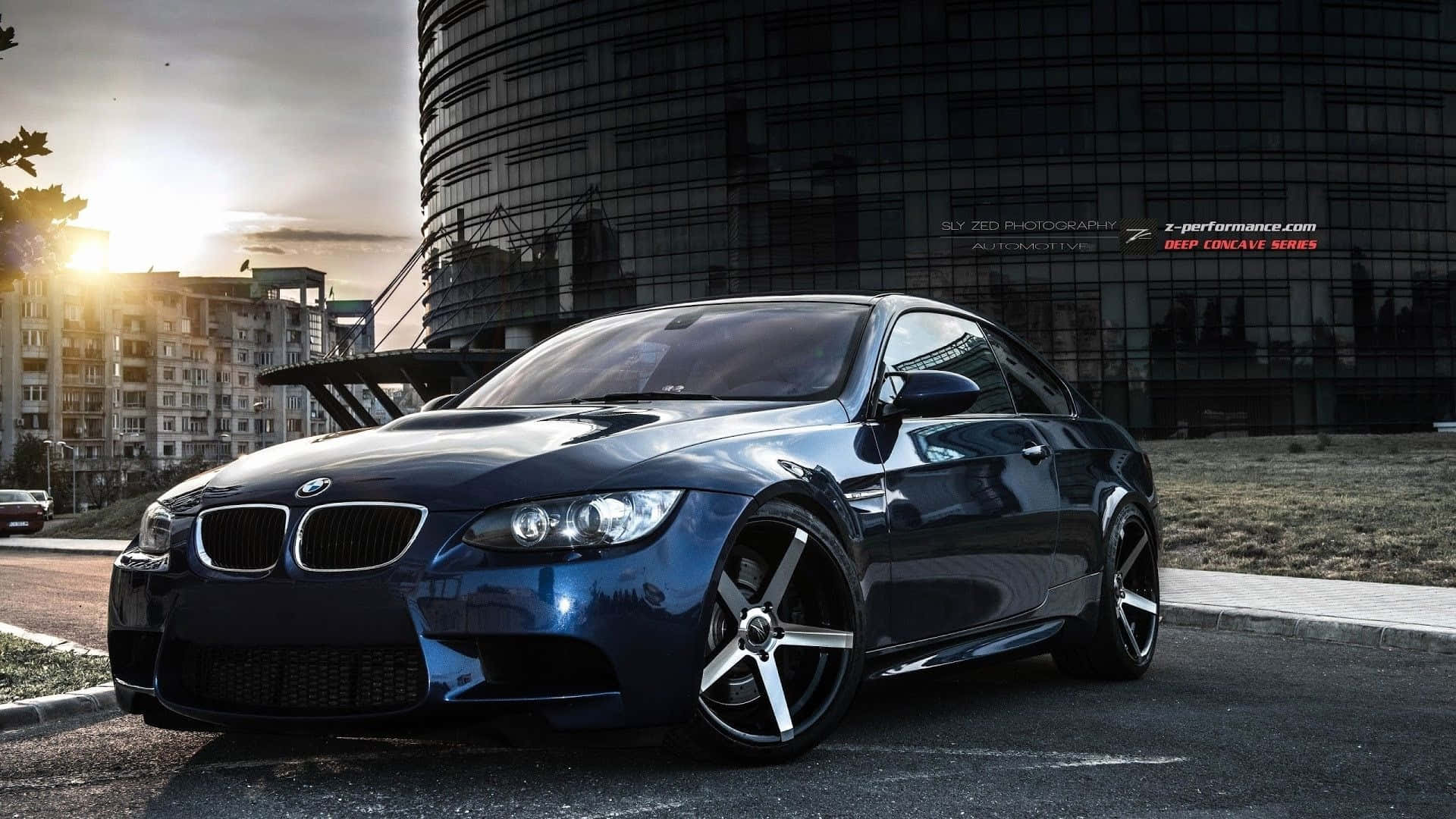 1920x1080 Bmw 桌布 壁紙 — 一架時尚深藍色BMW跑車停泊在日落時分的城市街道上，背後有一座現代玻璃建築。