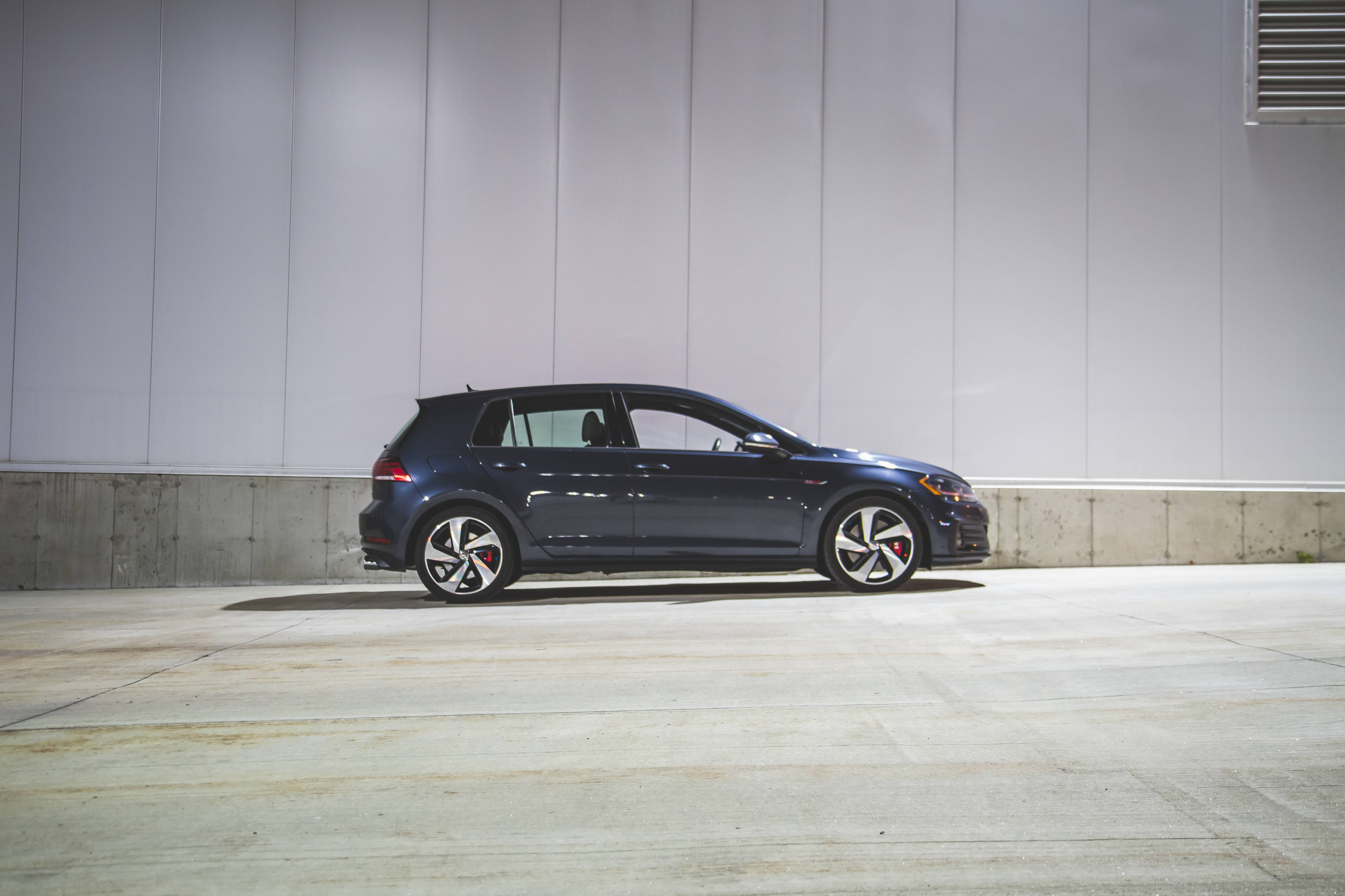 Gti 桌布 壁紙 — 一架時尚深藍色運動掀背車停放在簡約混凝土車庫，背景為純白牆壁。