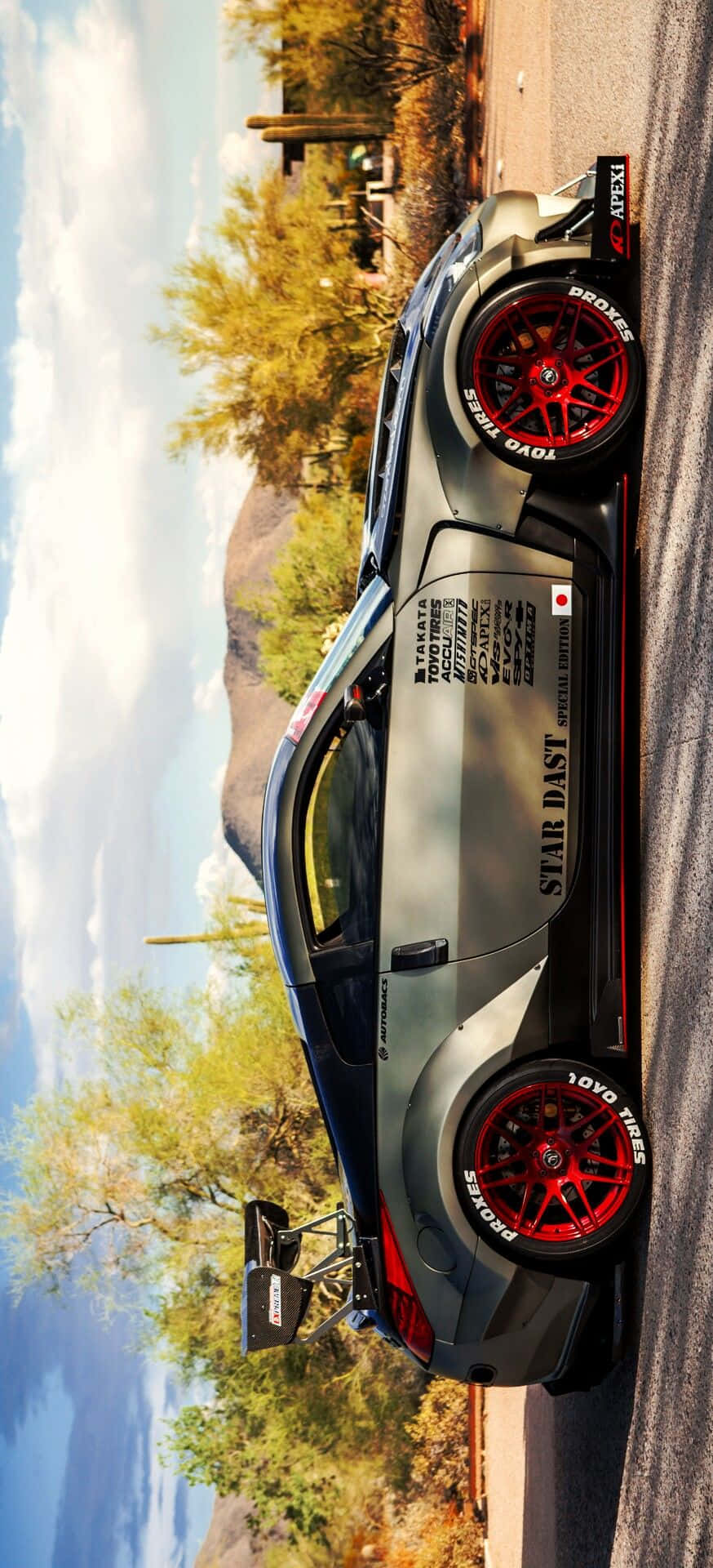 Nissan R35 Gtr 桌布 壁紙 — 一架時尚灰色賽車配紅色輪胎，停泊在沙漠公路旁，旁邊有仙人掌和山脈，天空局部多雲。