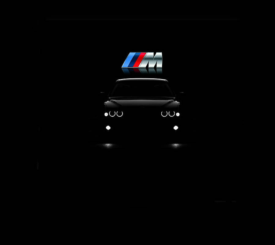 m 桌布 壁紙 — 一架時尚的BMW M車剪影在漆黑背景中閃爍著車頭燈，頂部有一個發光的M標誌。