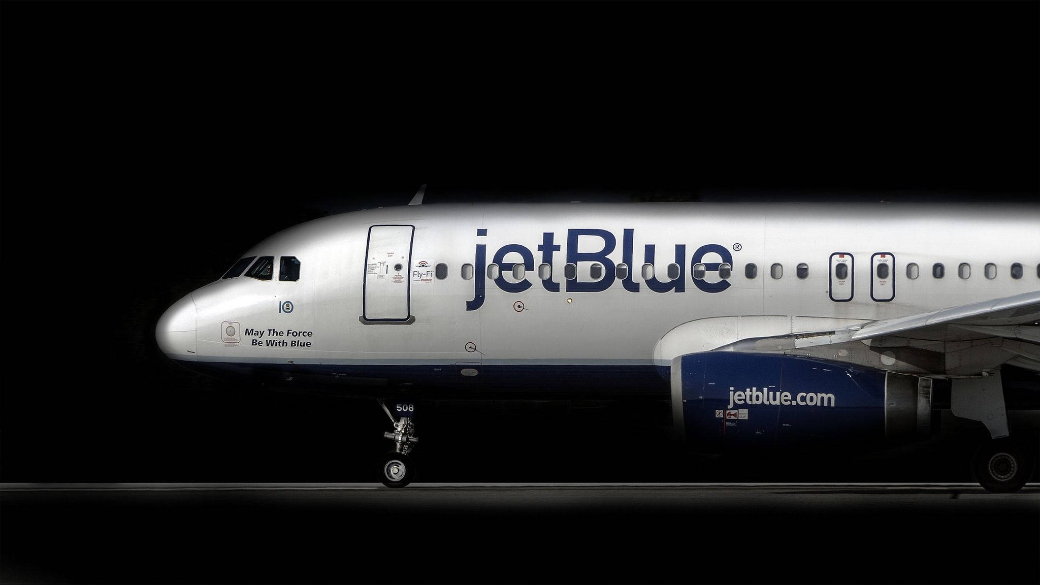 飛機 桌布 壁紙 — 一架時尚的jetBlue飛機在停機坪上，在聚光燈下對著漆黑的夜空發光。