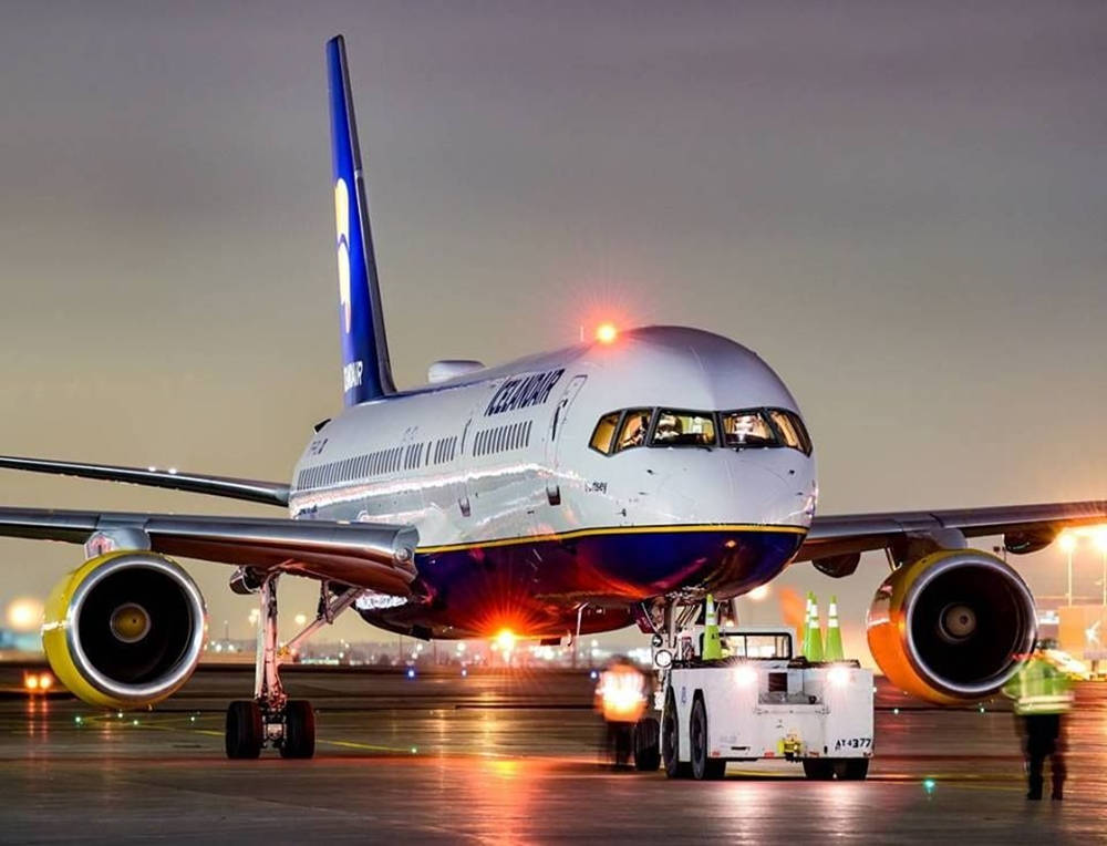 飛機 桌布 壁紙 — 一架時尚的冰島航空飛機在暮色燈光下閃耀，地勤人員在停機坪上推動它，引擎發光。
