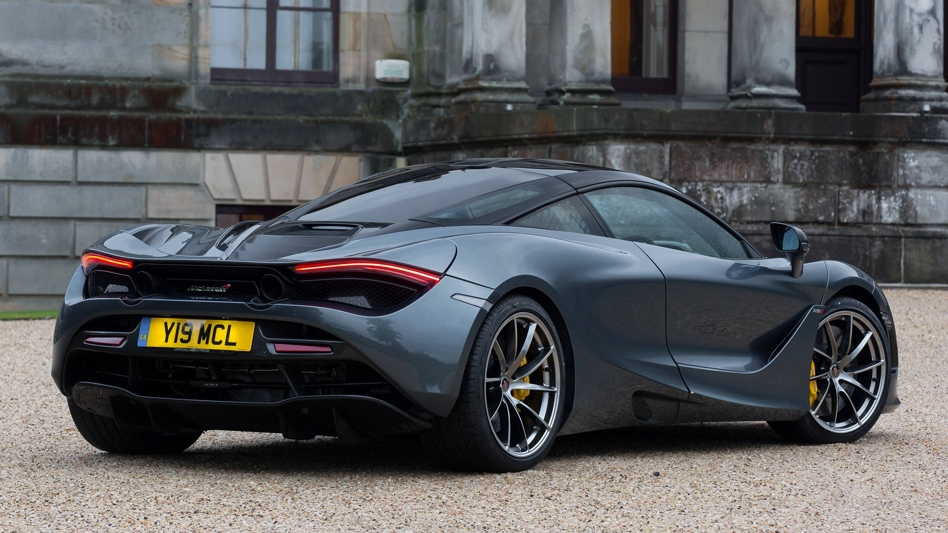 mclaren 720s 4K 桌布 壁紙 — 一架時尚的啞光灰色McLaren 720S跑車停泊在宏偉石建築前的碎石上。