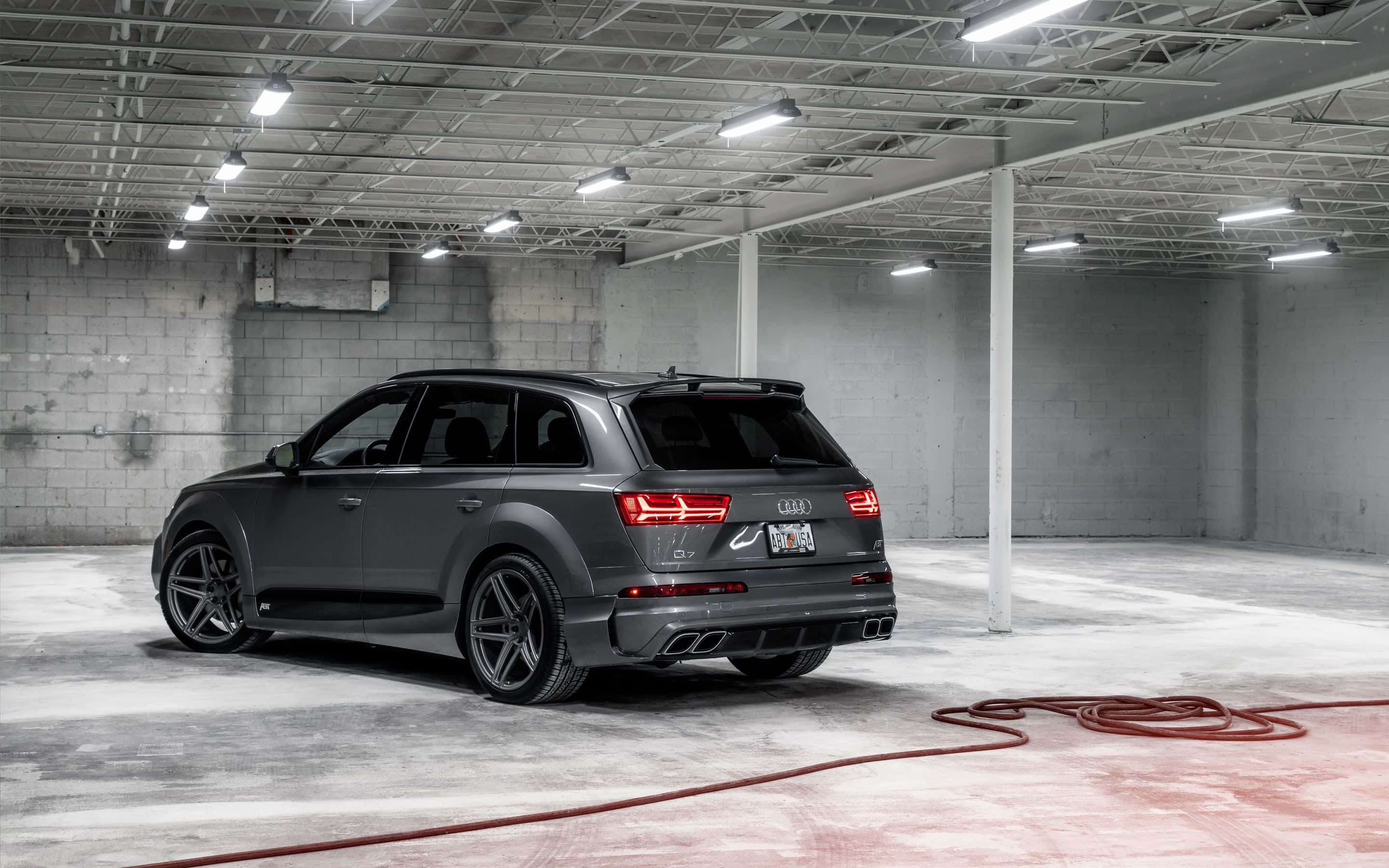 Audi Q7 桌布 壁紙 — 一架時尚的啞光灰色奧迪 SQ7 SUV 停放在簡約工業風車庫，車庫有裸露天花板橫樑和混凝土牆。