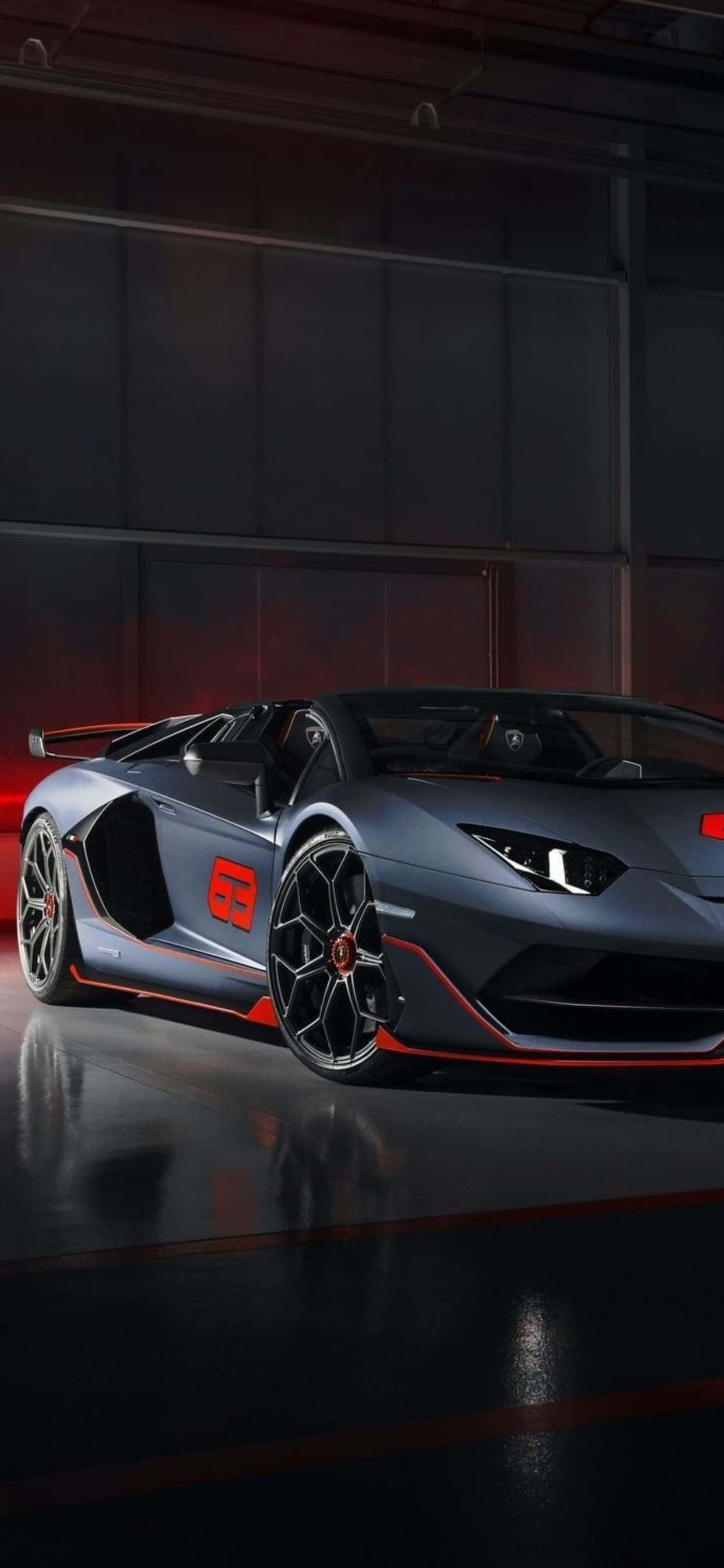 Lamborghini Phone 桌布 壁紙 — 一架時尚的啞光灰色藍寶堅尼Aventador，帶有鮮明的紅色點綴，在高科技車庫的戲劇性燈光下閃閃發光。