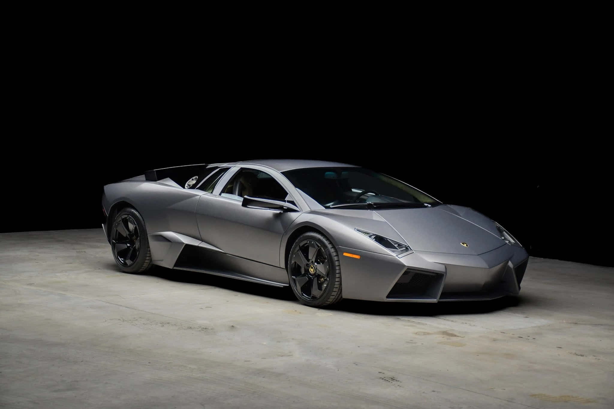 Lamborghini Reventón 桌布 壁紙 — 一架時尚的啞光銀色藍寶堅尼Reventon跑車在黑色背景下的混凝土地板上被戲劇性地照亮。