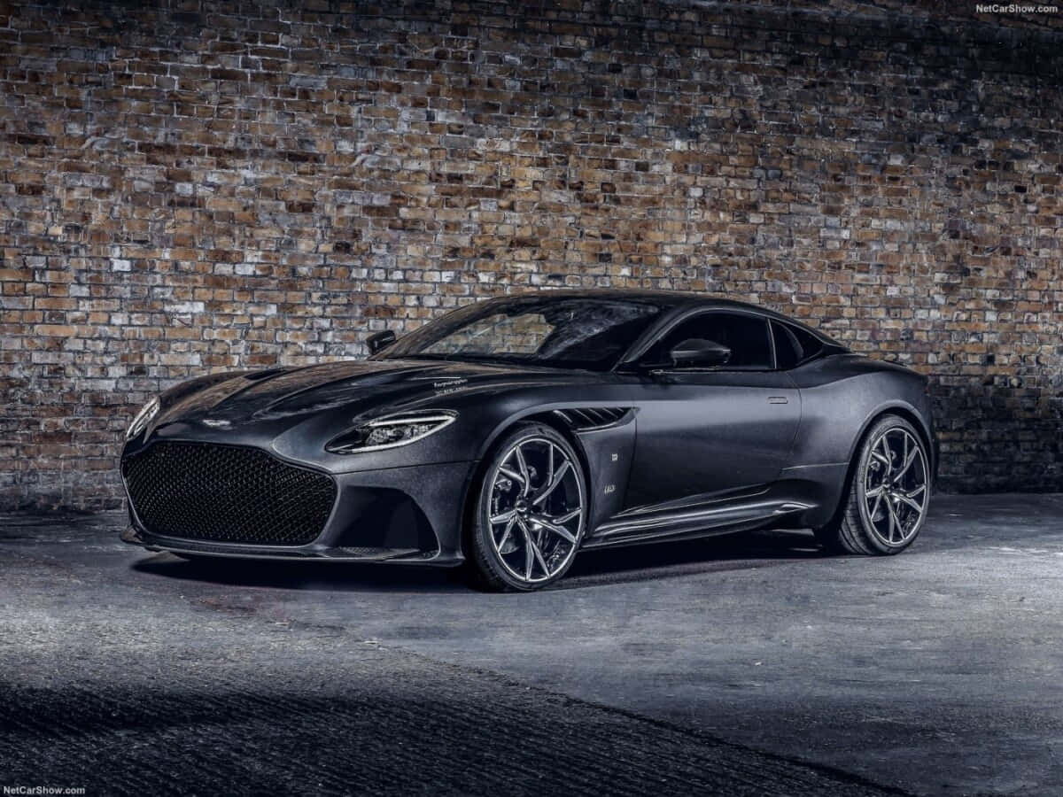 奧斯頓馬丁 桌布 壁紙 — 一架時尚的啞光黑色 Aston Martin DBS Superleggera 停在風化的磚牆前，燈光效果戲劇化。