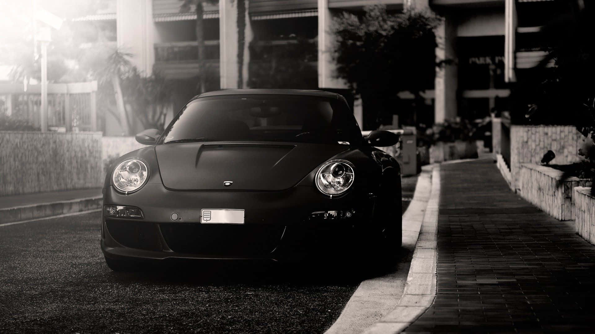 Black And White Car 桌布 壁紙 — 一架時尚的啞光黑色跑車停泊在陽光明媚的城市街道上，背景有棕櫚樹和建築物。