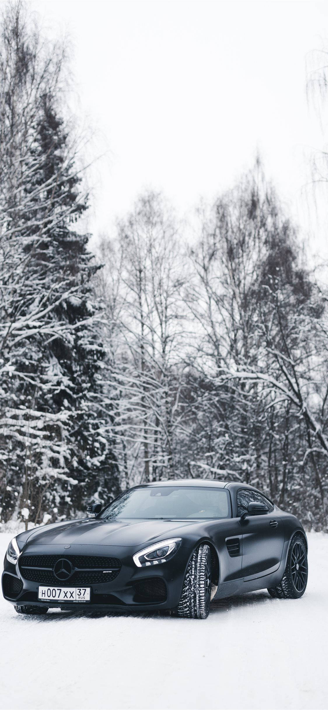 ford iPhone 桌布 壁紙 — 一架時尚的啞光黑色跑車停泊在雪地森林中，周圍是白雪覆蓋的樹木，天空多雲。