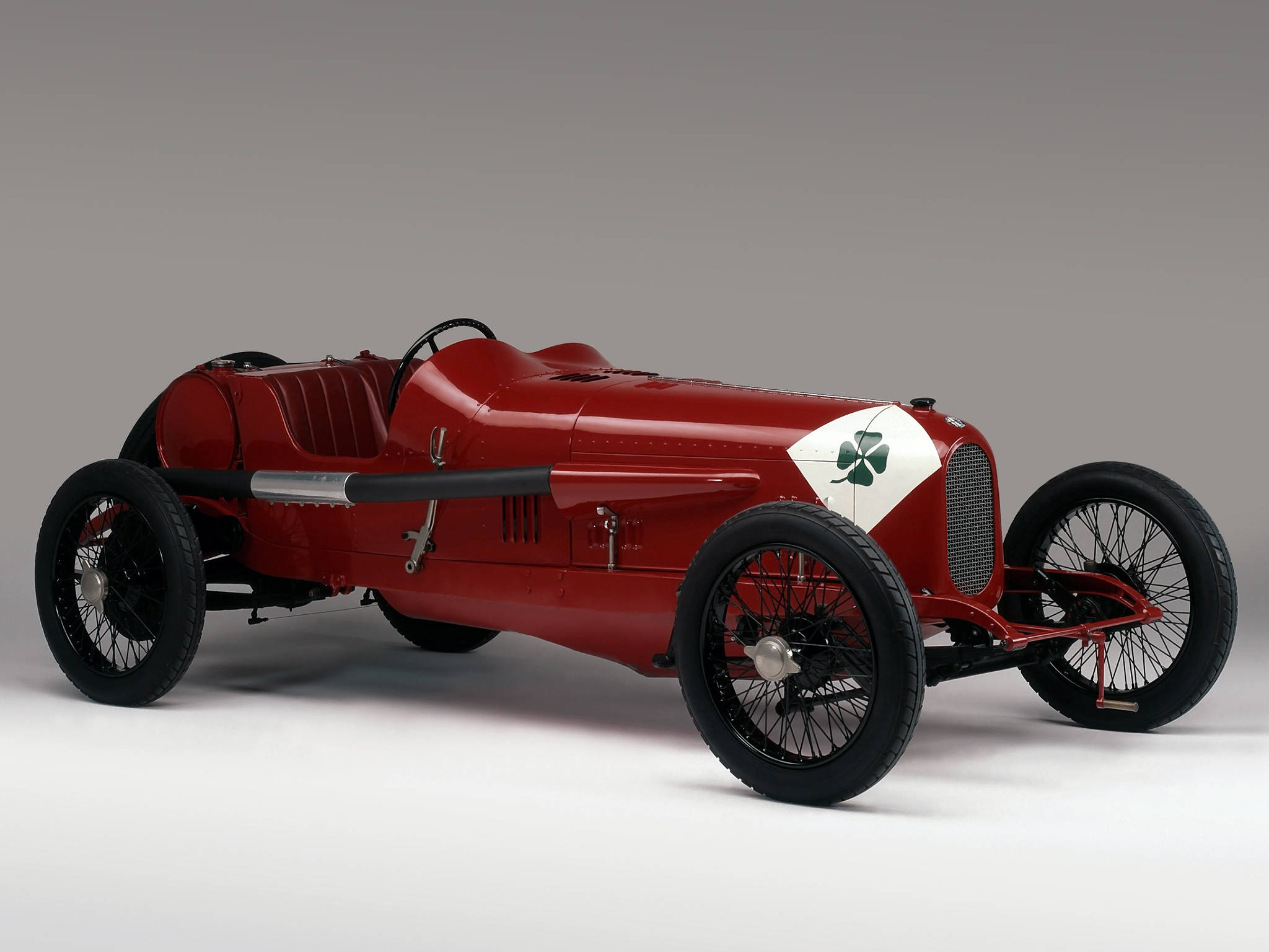 alfa romeo iPhone 桌布 壁紙 — 一架時尚的復古紅色賽車，帶有白色面板和綠色三葉草標誌，在中性工作室背景前蓄勢待發。