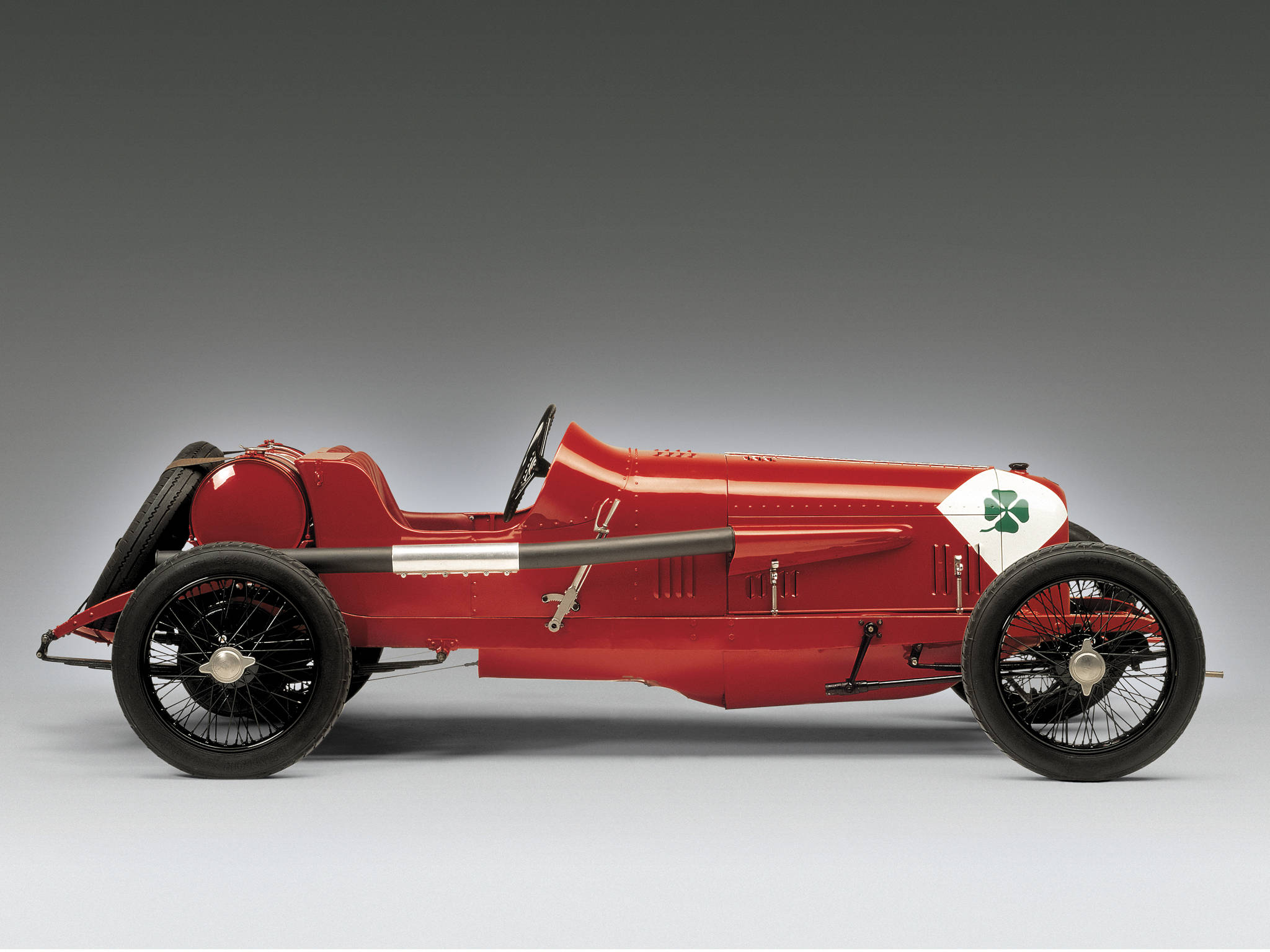 alfa romeo iPhone 桌布 壁紙 — 一架時尚的復古紅色賽車，帶有白色面板和綠色三葉草標誌，在中性工作室背景前蓄勢待發。