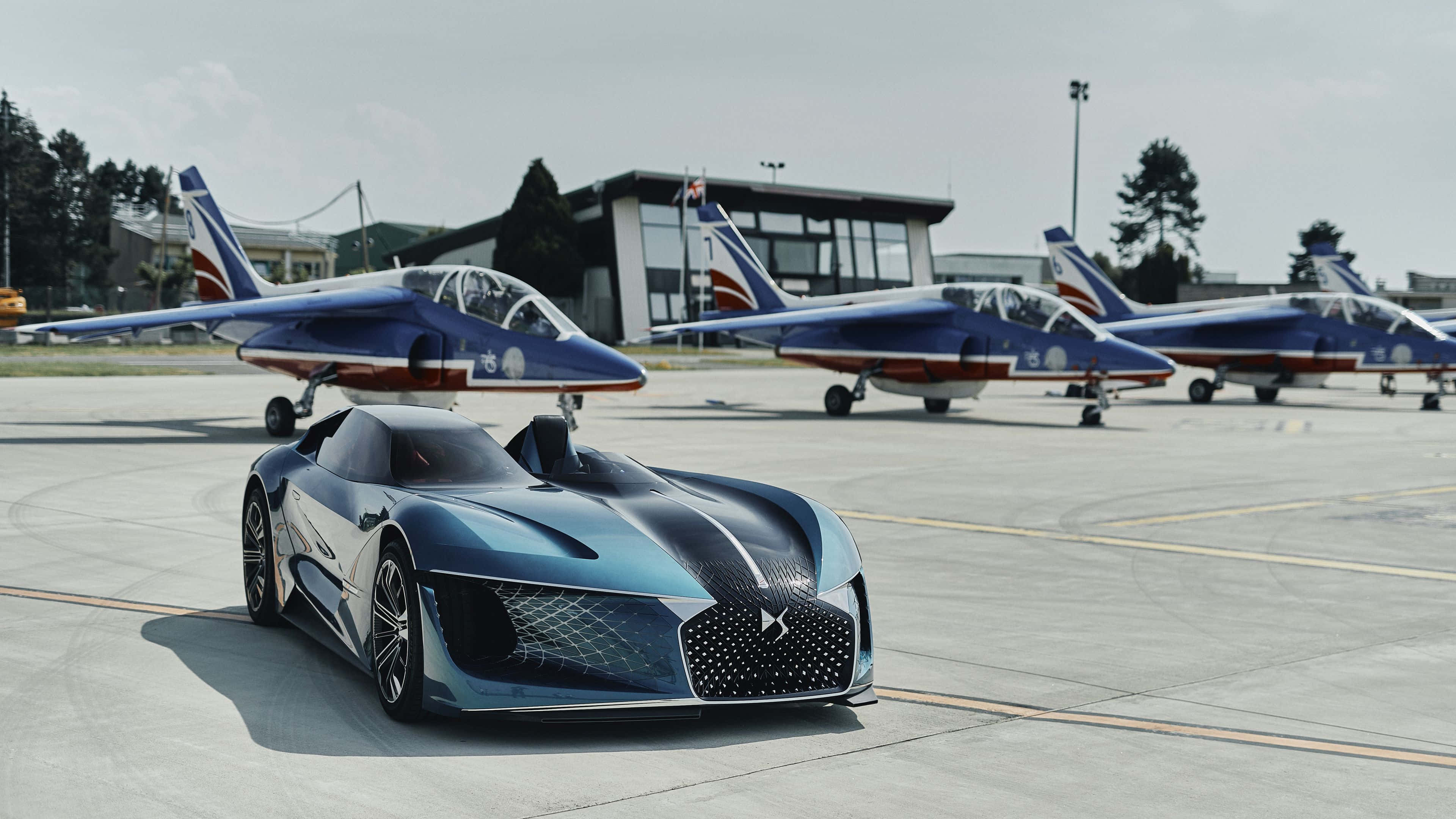 Ds Automobiles 桌布 壁紙 — 一架時尚的未來感藍色跑車停泊在機場，背後有三架藍色和橙色的戰鬥機排列著。