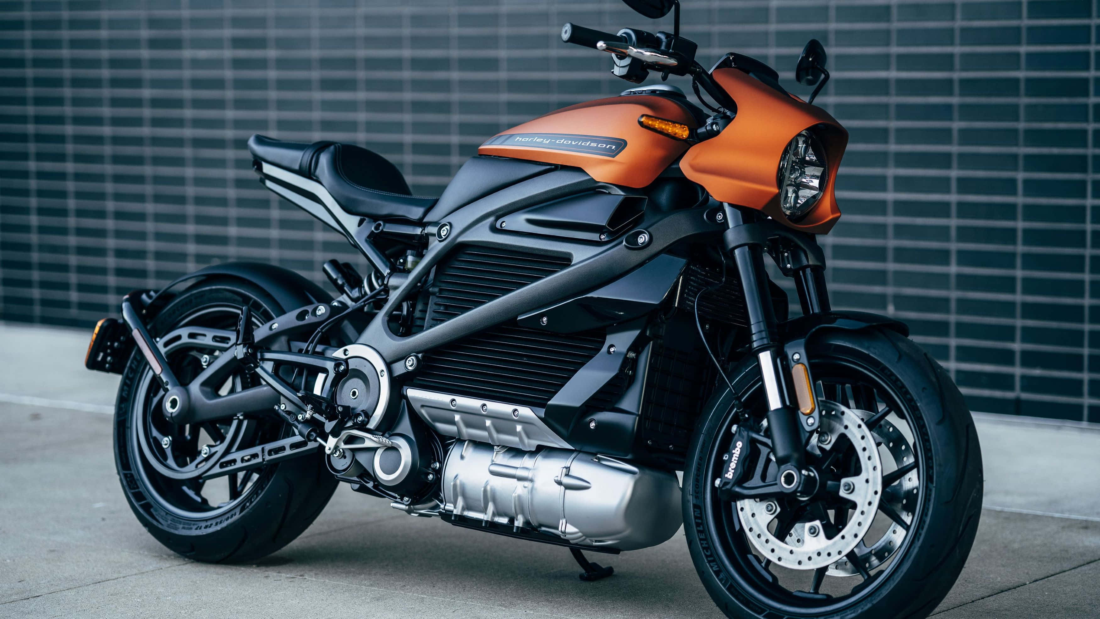 Electric Bike 桌布 壁紙 — 一架時尚的橙色和黑色Harley-Davidson電動機車停放在深灰色瓷磚牆前。