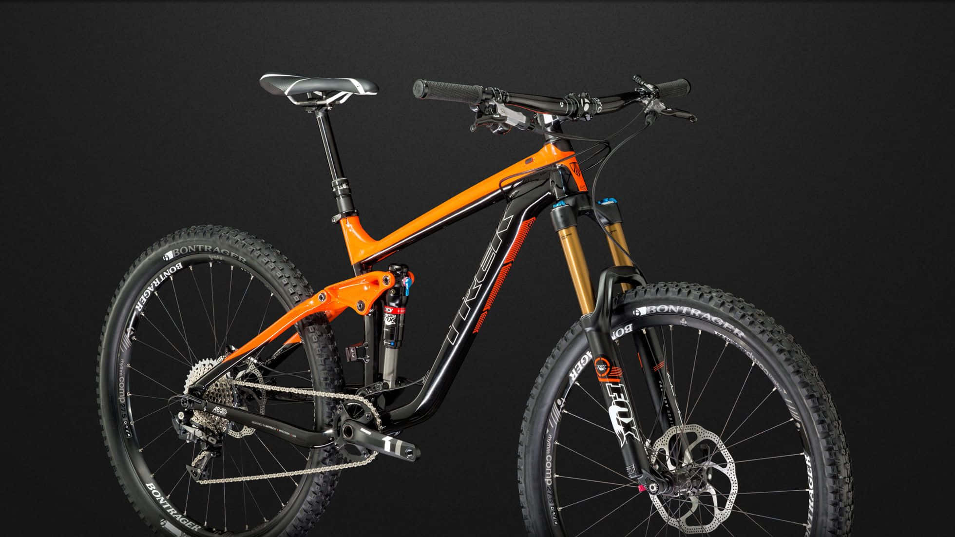 Bikes 桌布 壁紙 — 一架時尚的橙色和黑色全避震登山車，配備金色前叉，在深色攝影棚背景前矗立。