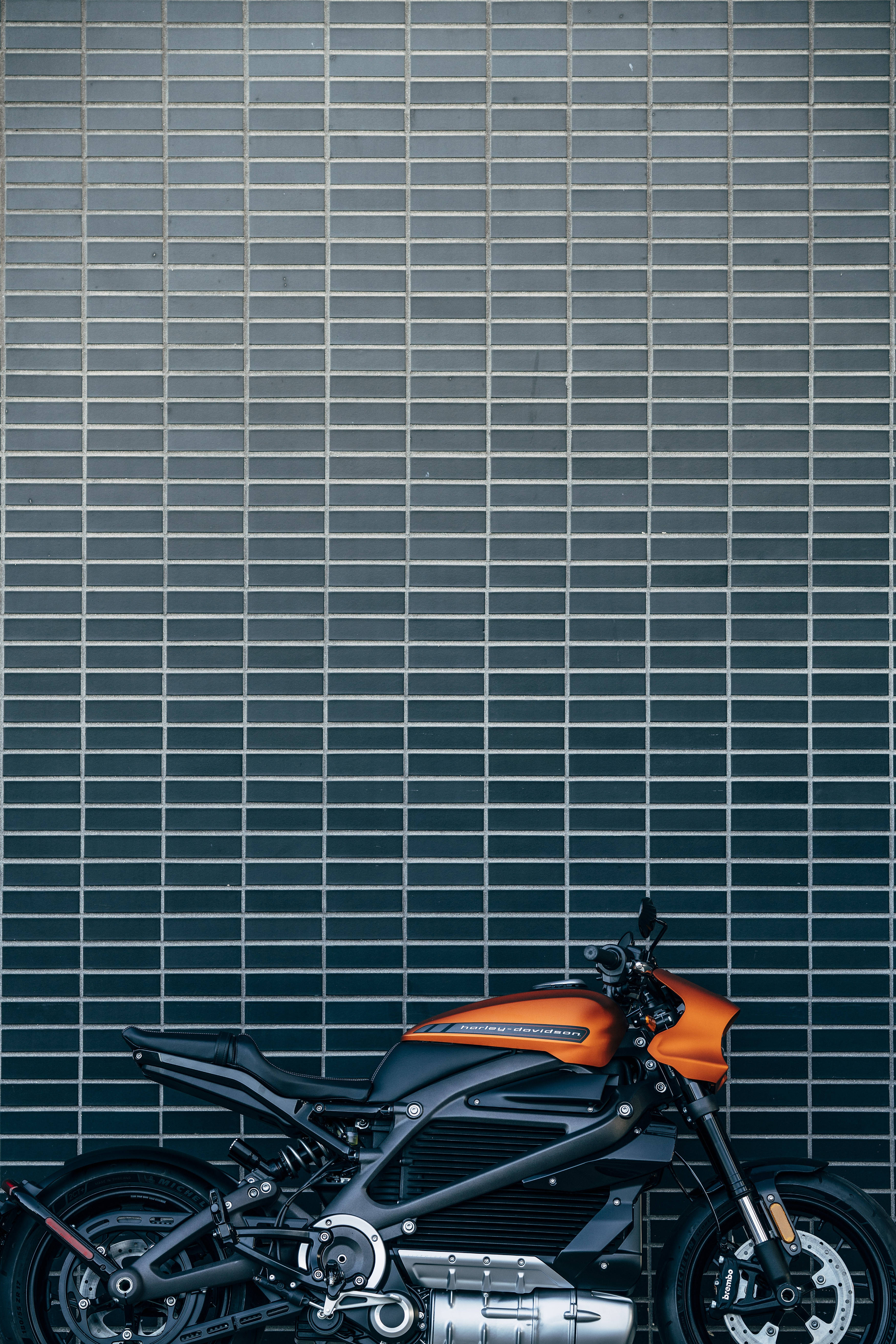 Harley 桌布 壁紙 — 一架時尚的橙色和黑色電動機車靠著深灰色瓷磚牆，帶有白色填縫線。