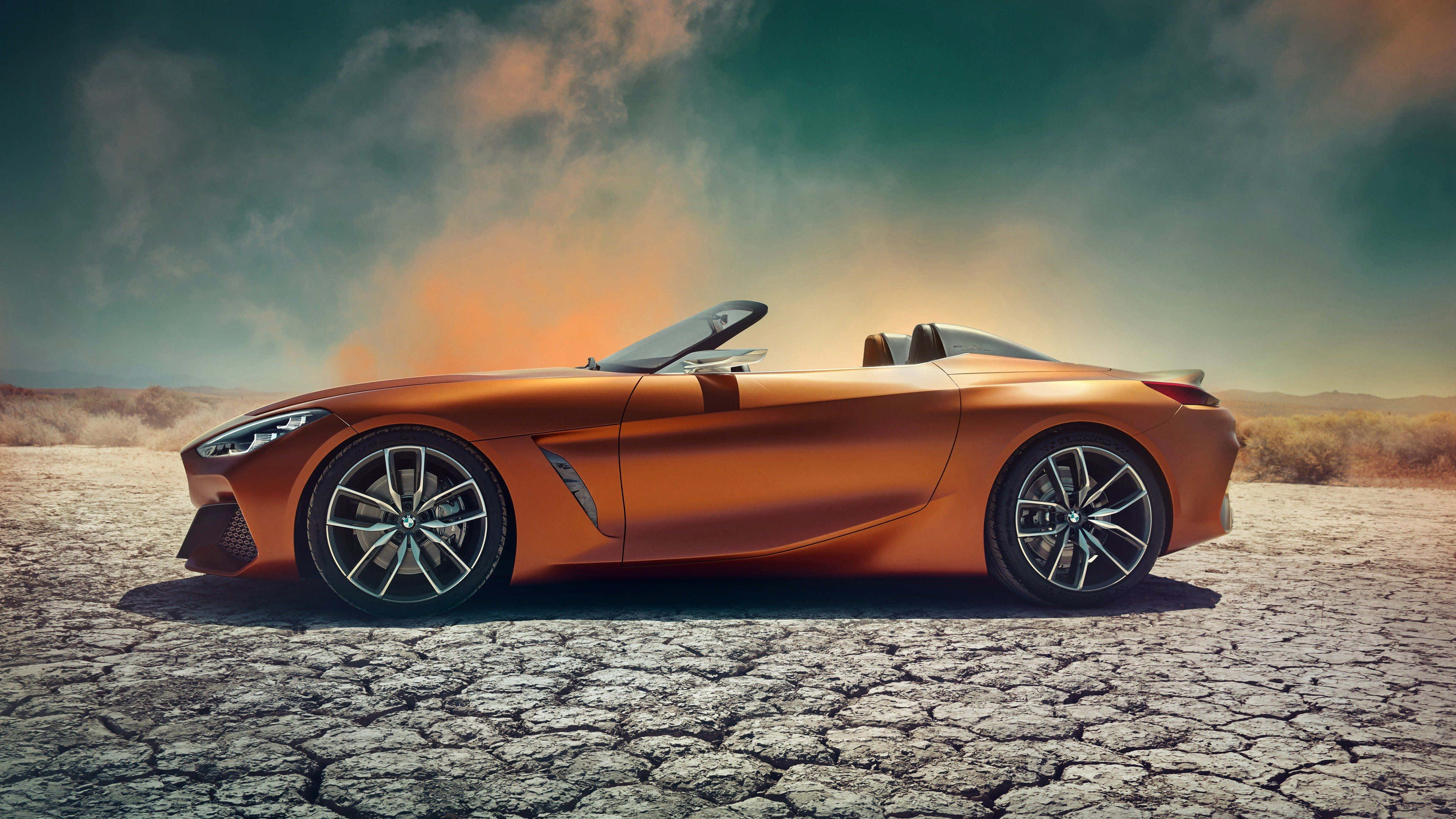 Bmw Z4 桌布 壁紙 — 一架時尚的橙色敞篷跑車停放在龜裂的沙漠土地上，背景是戲劇性的暮色天空。