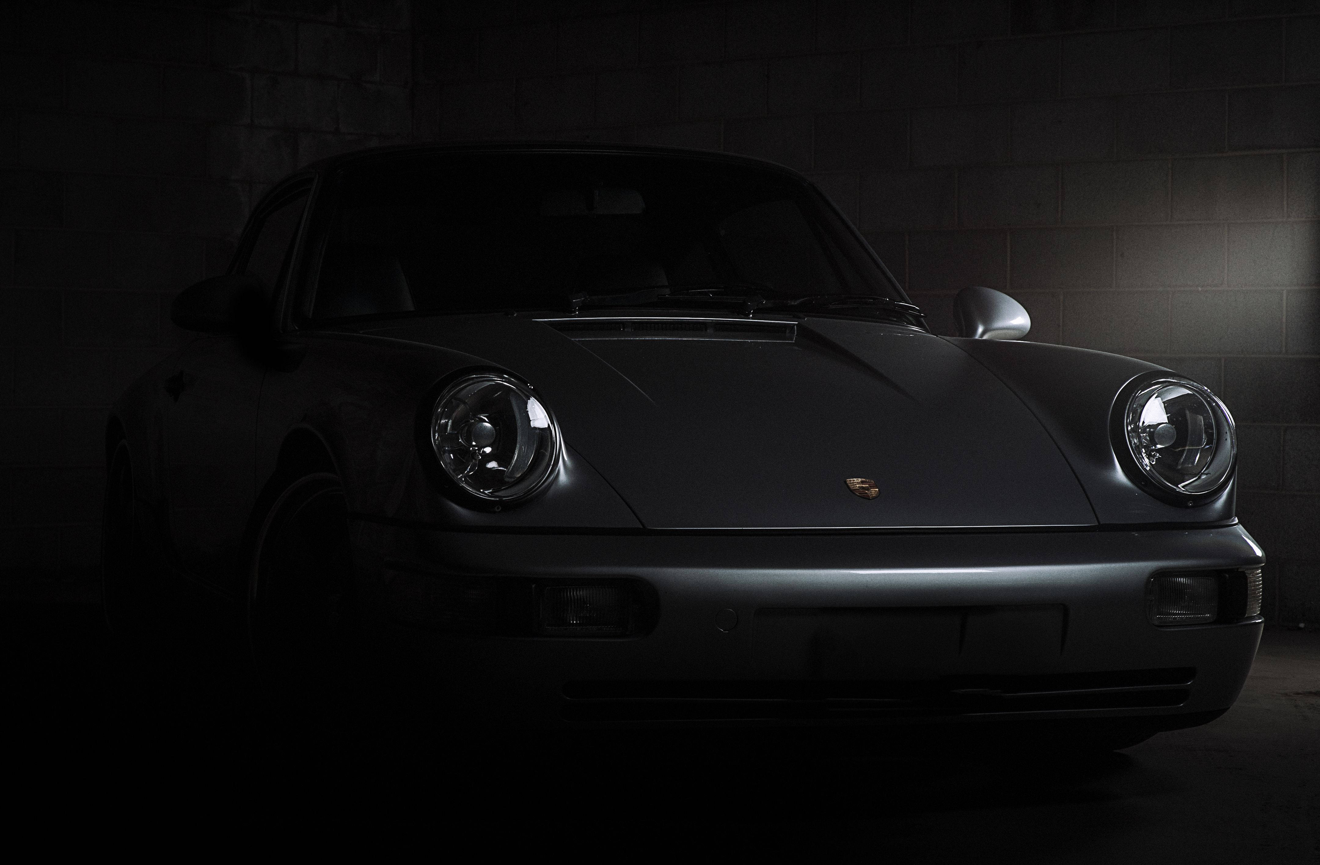 Porsche 911 桌布 壁紙 — 一架時尚的消光灰保時捷911在昏暗的混凝土車庫中被戲劇性地照亮，凸顯其標誌性圓形頭燈和曲線。