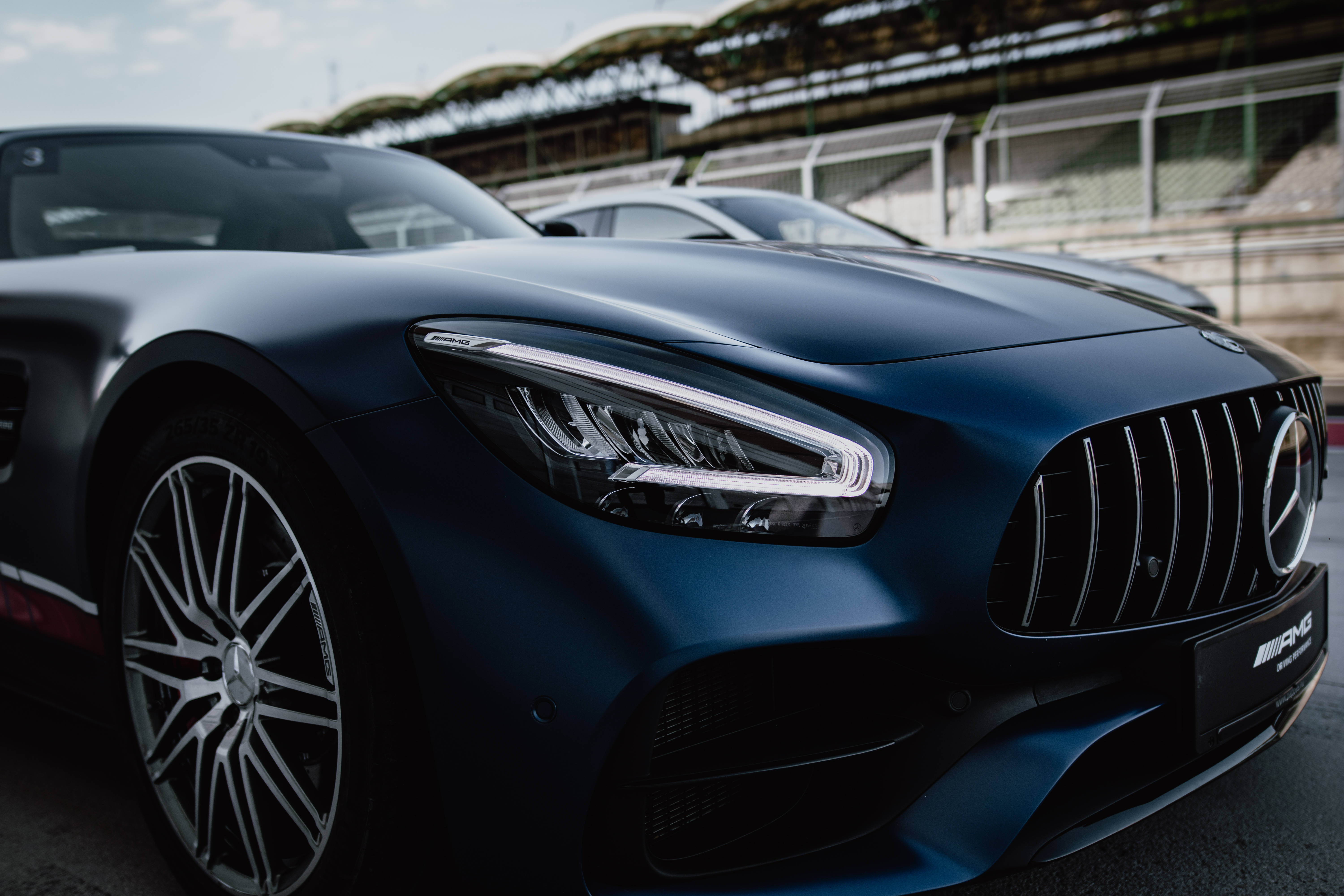 amg iPhone 桌布 壁紙 — 一架時尚的消光藍色 Mercedes-AMG GT 停在賽車場上，背景是看台。