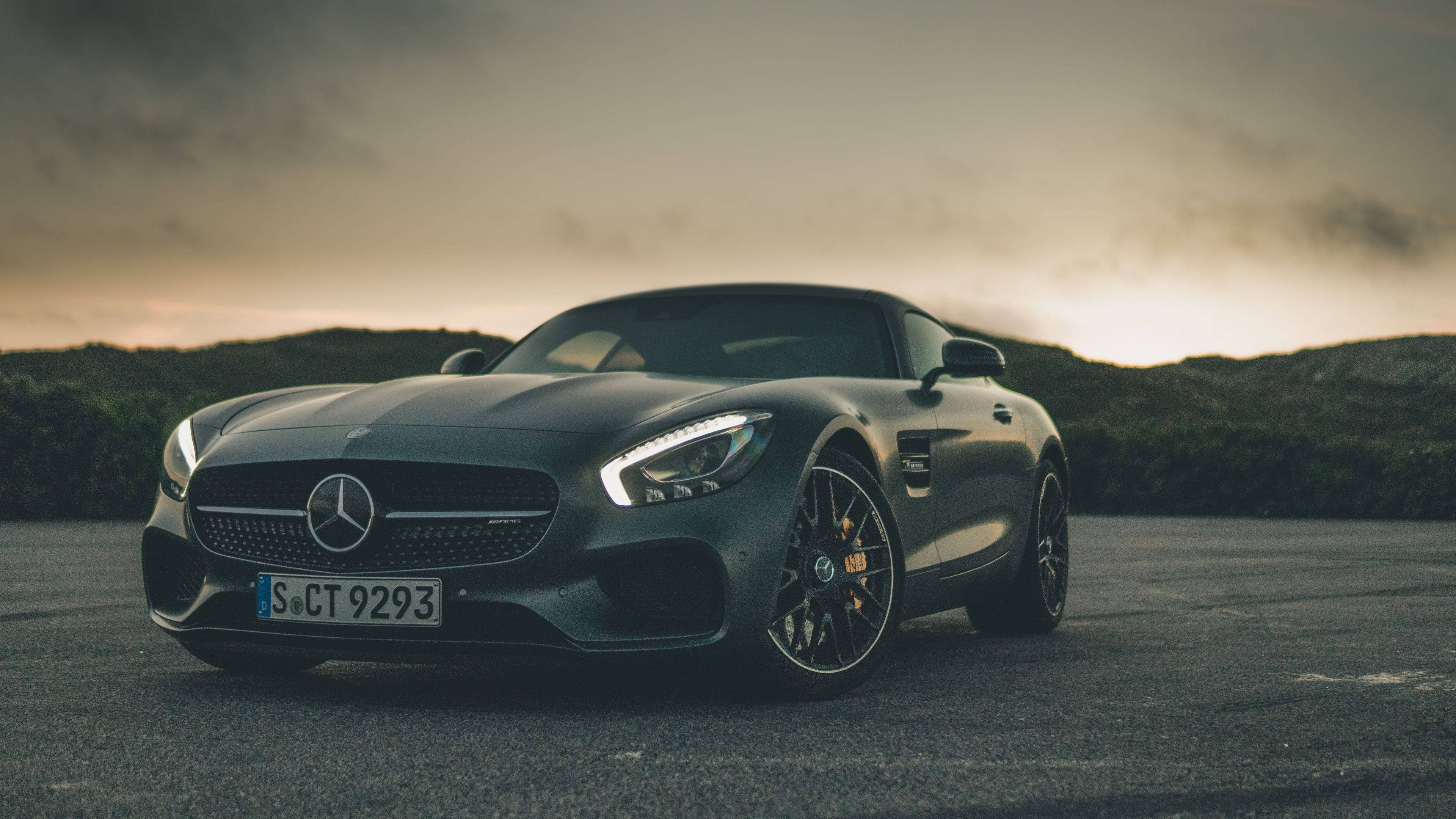 Mercedes 桌布 壁紙 — 一架時尚的消光黑色 Mercedes-AMG GT 跑車停在日落時分的柏油路上，背景有山丘。