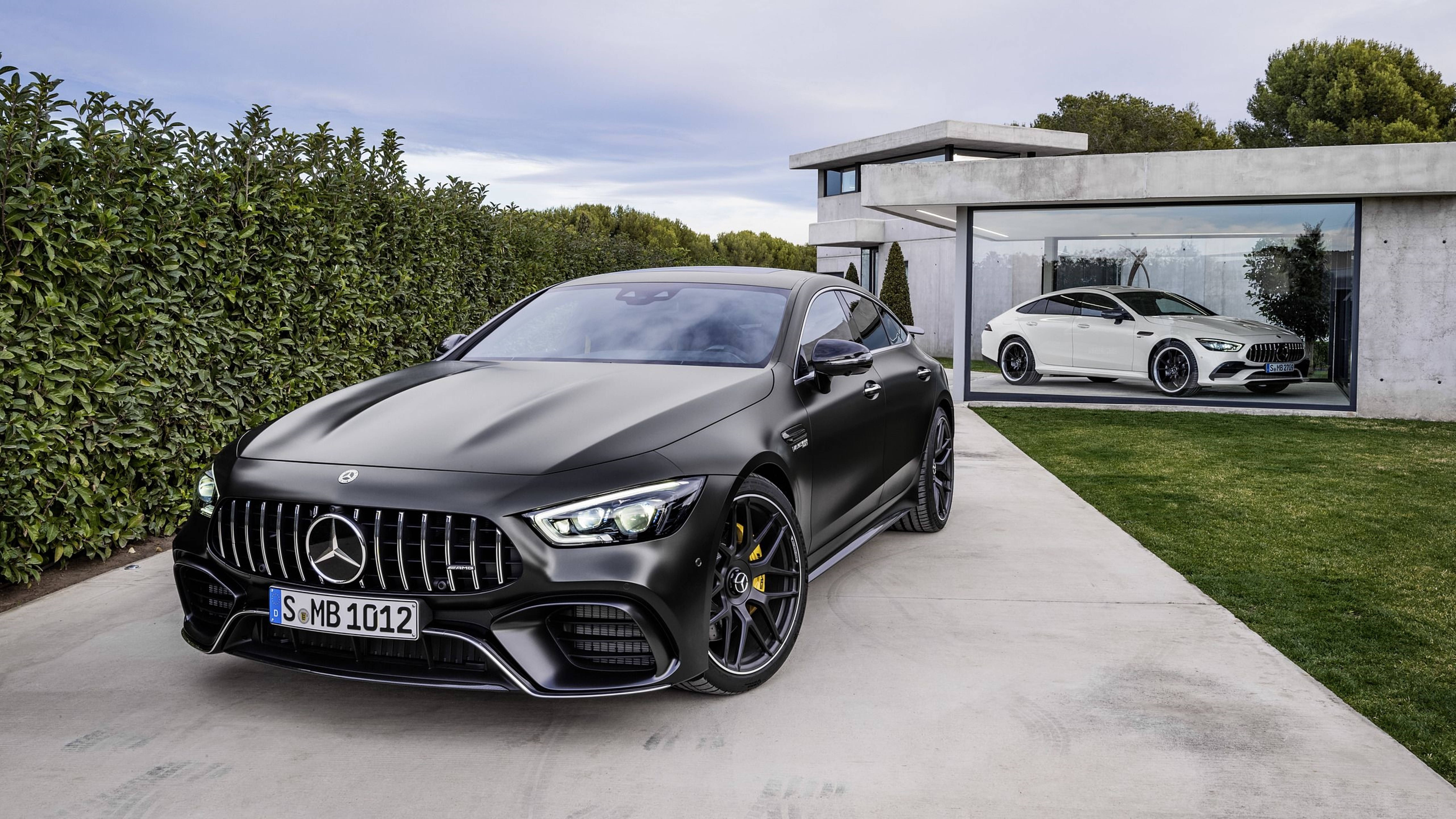 消光黑色 Mercedes-AMG GT 停放在現代玻璃車庫外，車庫內有一架白色 AMG GT。 — 4K 奔馳壁紙 壁紙