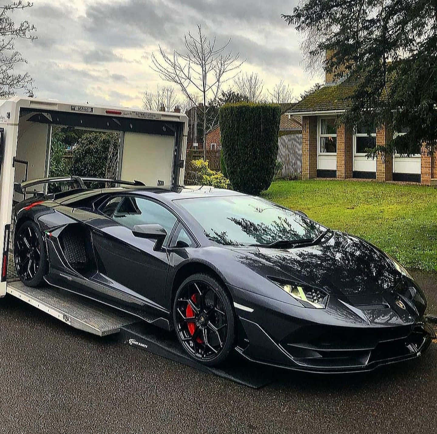 race car 桌布 壁紙 — 一架時尚的消光黑色藍寶堅尼Aventador停在郊區車道的拖車上，天空陰沉。