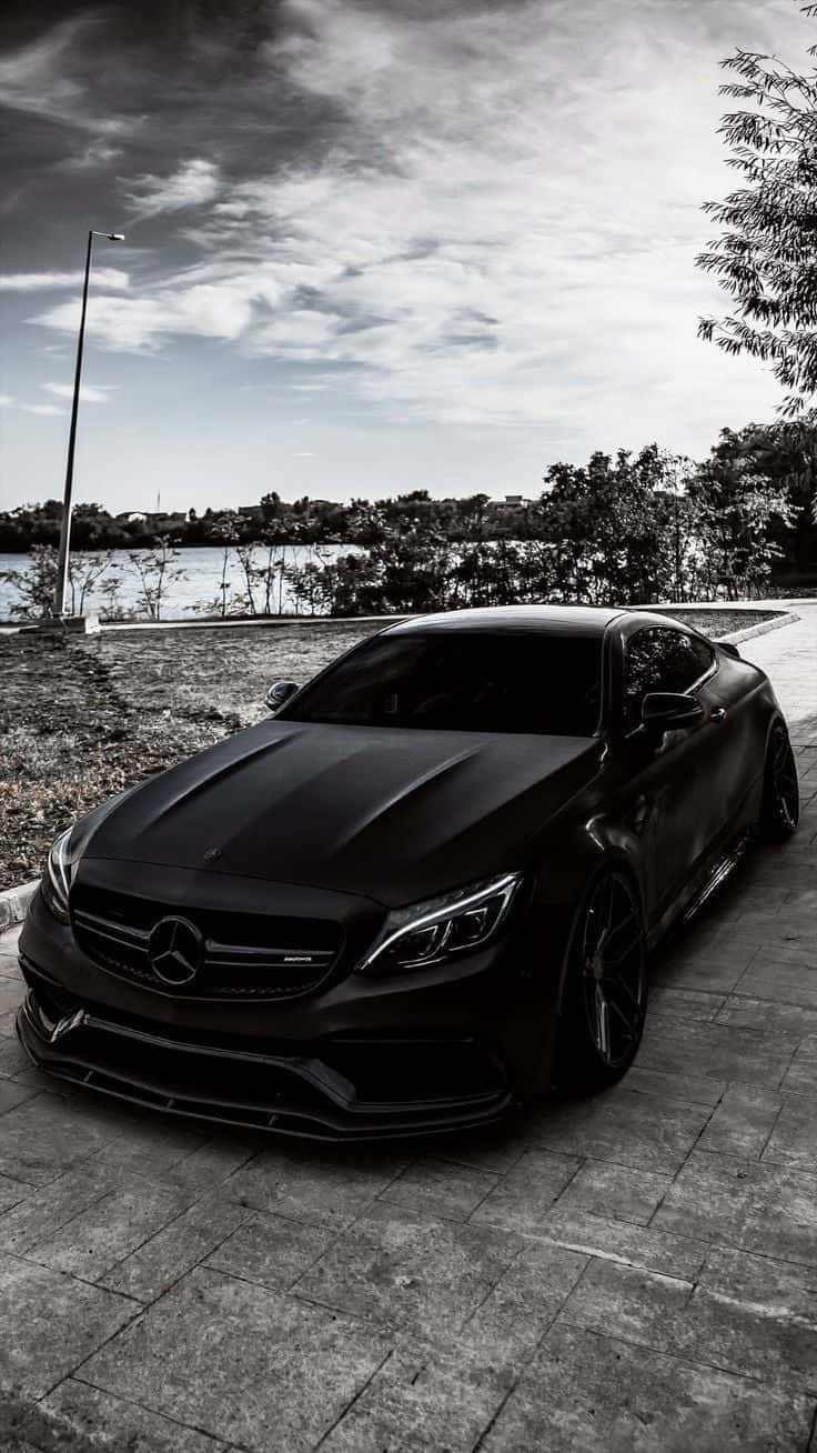 Mercedes 桌布 壁紙 — 一架時尚的消光黑色賓士跑車停泊在石徑上，旁邊是平靜的湖泊，天空多雲。
