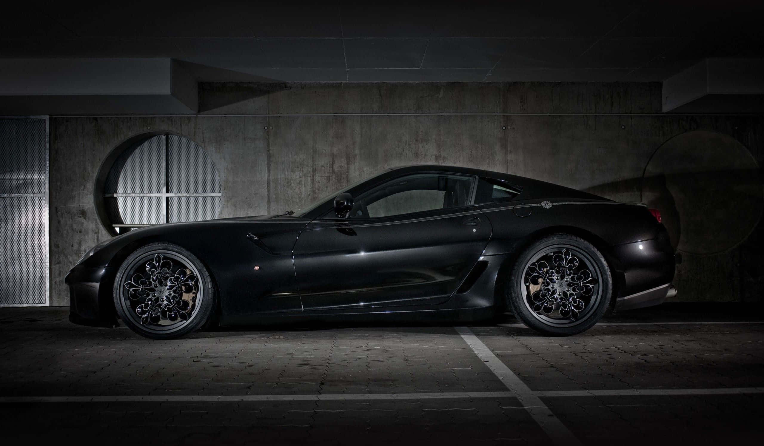 Ferrari 599 Gtb Fiorano 桌布 壁紙 — 一架時尚的消光黑色跑車停放在光線昏暗的混凝土車庫中，帶有戲劇性的聚光燈照明。