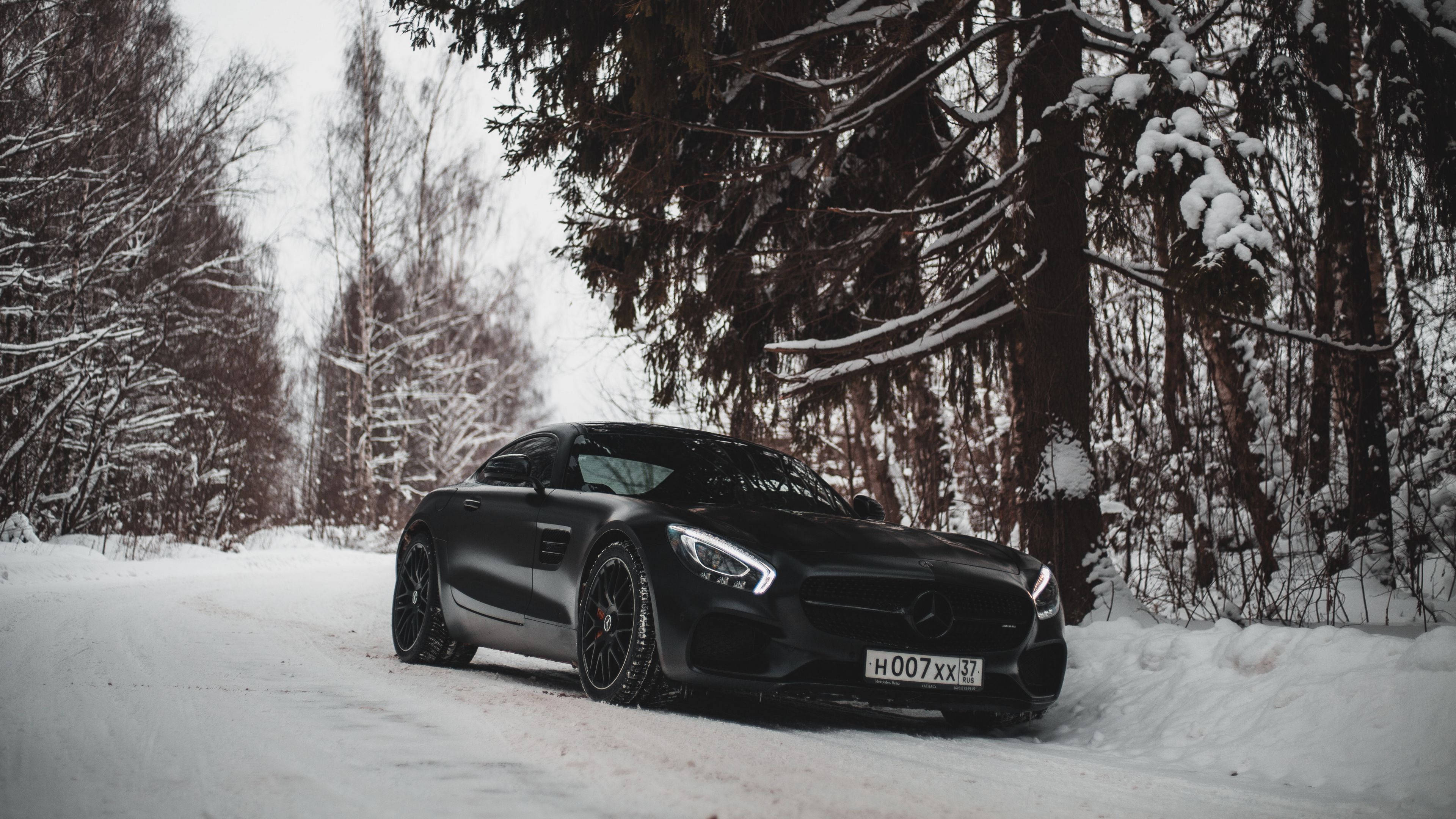 benz 4K 桌布 壁紙 — 一架時尚的消光黑色跑車停泊在白雪覆蓋的森林道路上，周圍是積雪的樹木。