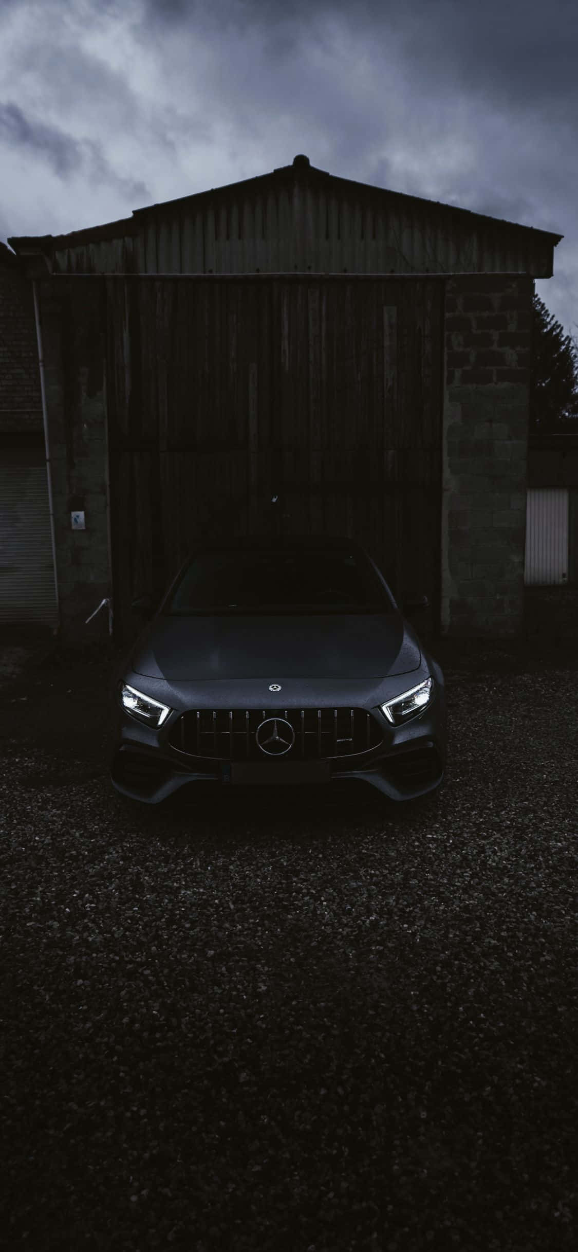 跑車 桌布 壁紙 — 一架時尚的深灰色 Mercedes-AMG 跑車在風雨交加的天空下，於一間風化的穀倉前，在車頭燈下閃耀。