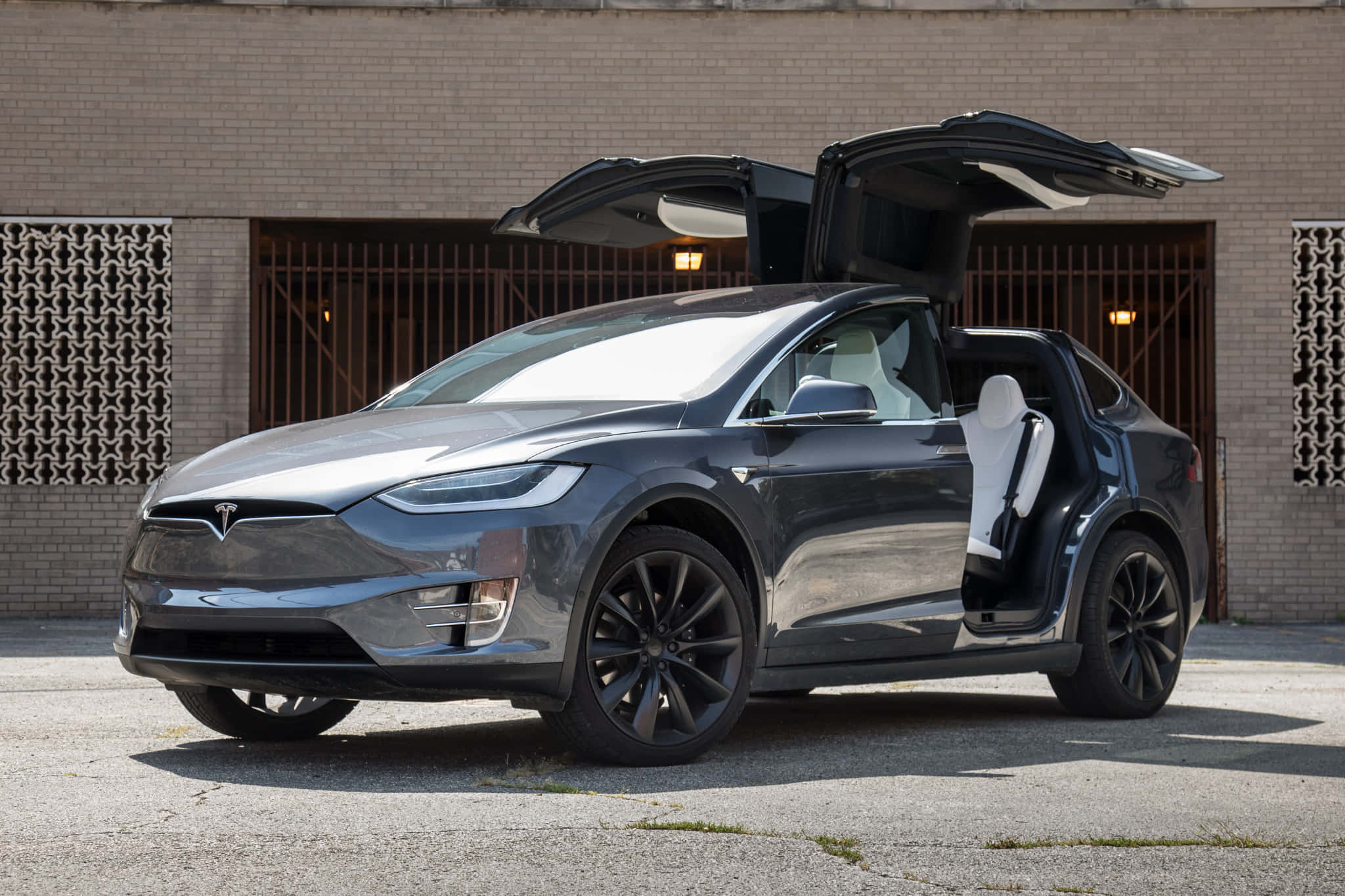 特斯拉 桌布 壁紙 — 一架時尚的深灰色 Tesla Model X 展開鷹翼門，停在磚砌建築前的鋪砌場地上。