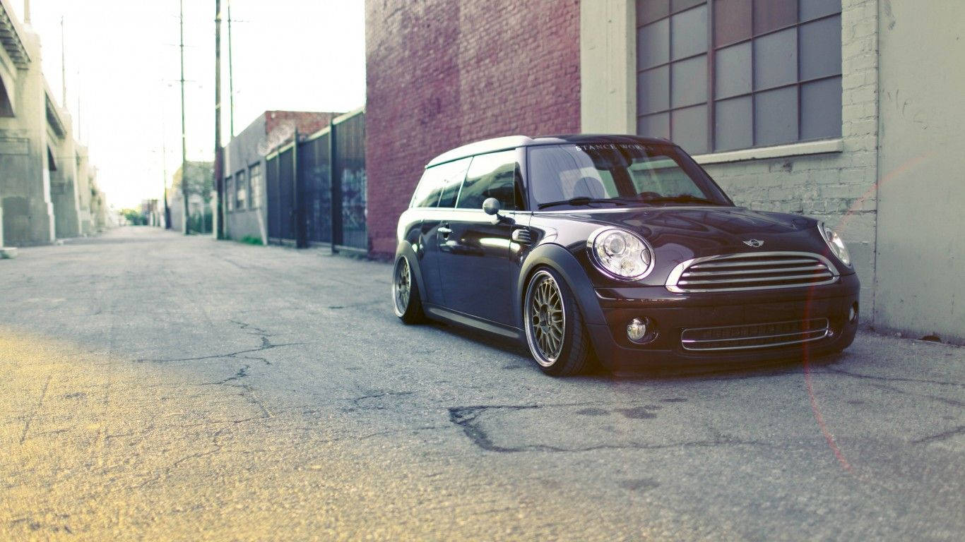 Mini Cooper 桌布 壁紙 — 一架時尚的深紫色MINI旅行車停放在陽光明媚的城市小巷中，旁邊是磚砌建築。