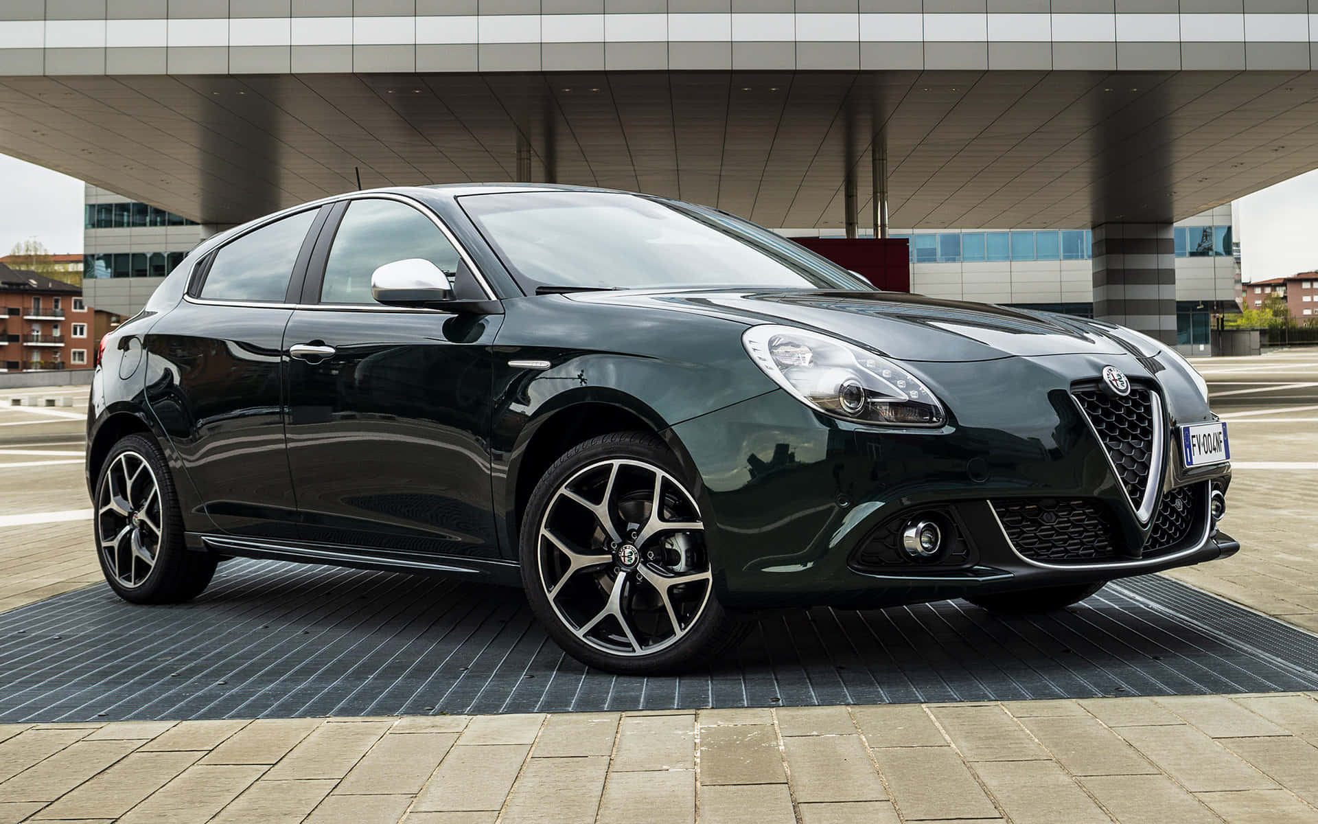 Alfa Romeo Giulietta 桌布 壁紙 — 一架時尚的深綠色愛快羅密歐Giulietta停放在現代建築簷篷下的鋪砌廣場上。