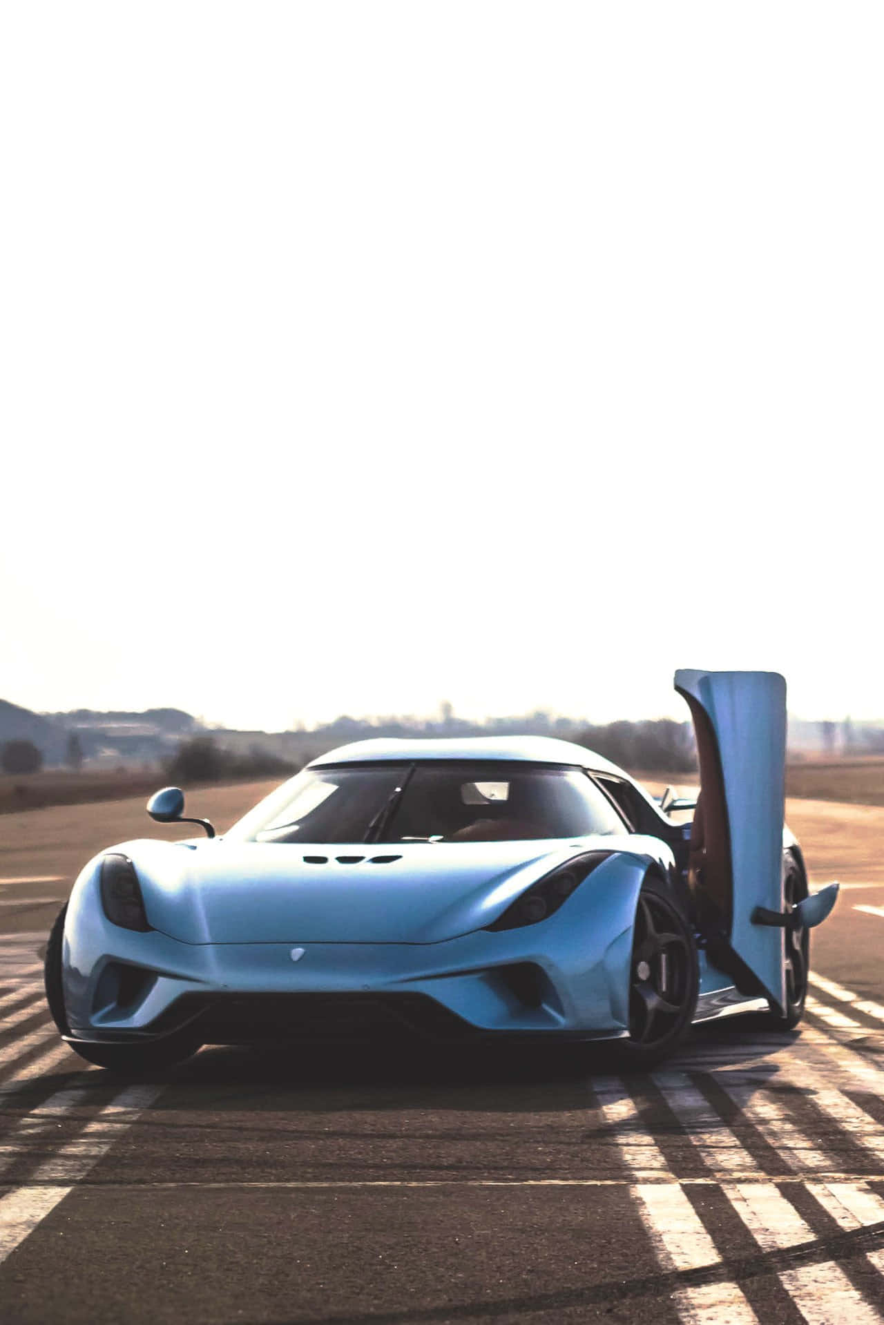 Koenigsegg 桌布 壁紙 — 一架時尚的淺藍色 Koenigsegg 超跑打開車門，停在陽光普照的賽道上，投下清晰的陰影。