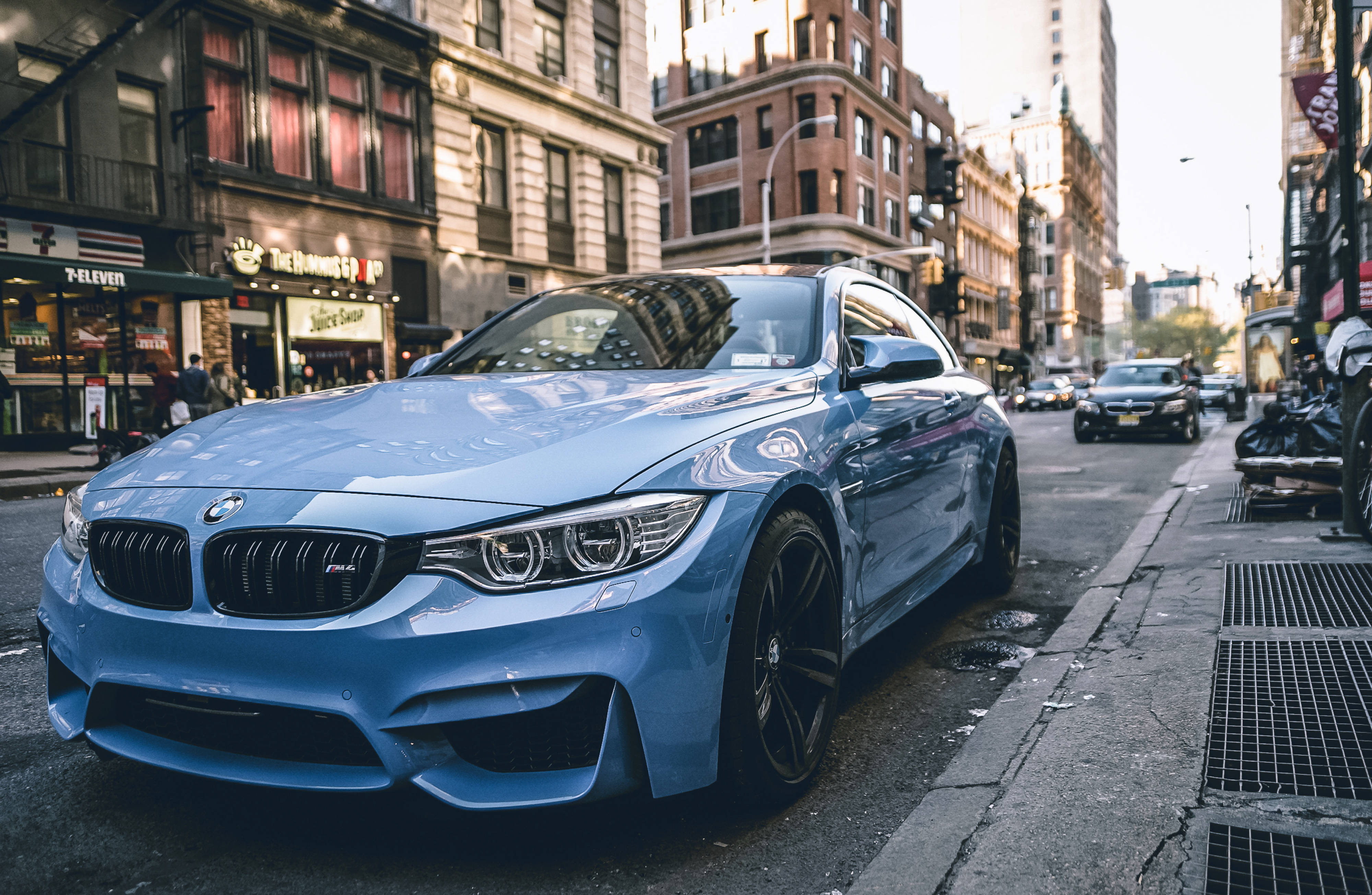 4K BMW 壁紙 桌布 壁紙 — 一架時尚的淺藍色BMW M4雙門跑車停放在陽光普照的都市街道上，背景是磚造建築和商店門面。