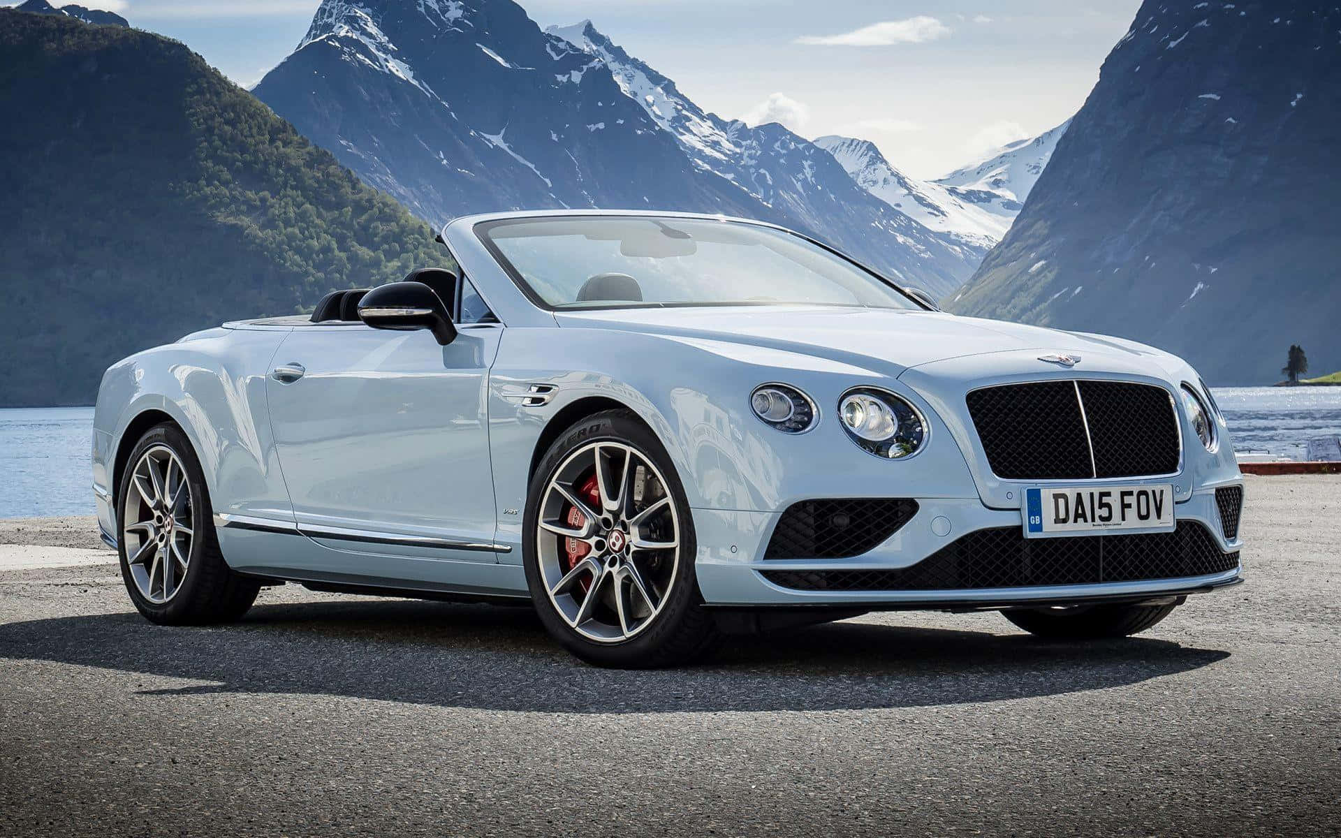 Bentley Continental Gt Convertible 桌布 壁紙 — 一架時尚的淺藍色賓利敞篷車停在鋪砌的道路上，背景是白雪覆蓋的山脈和湖泊。