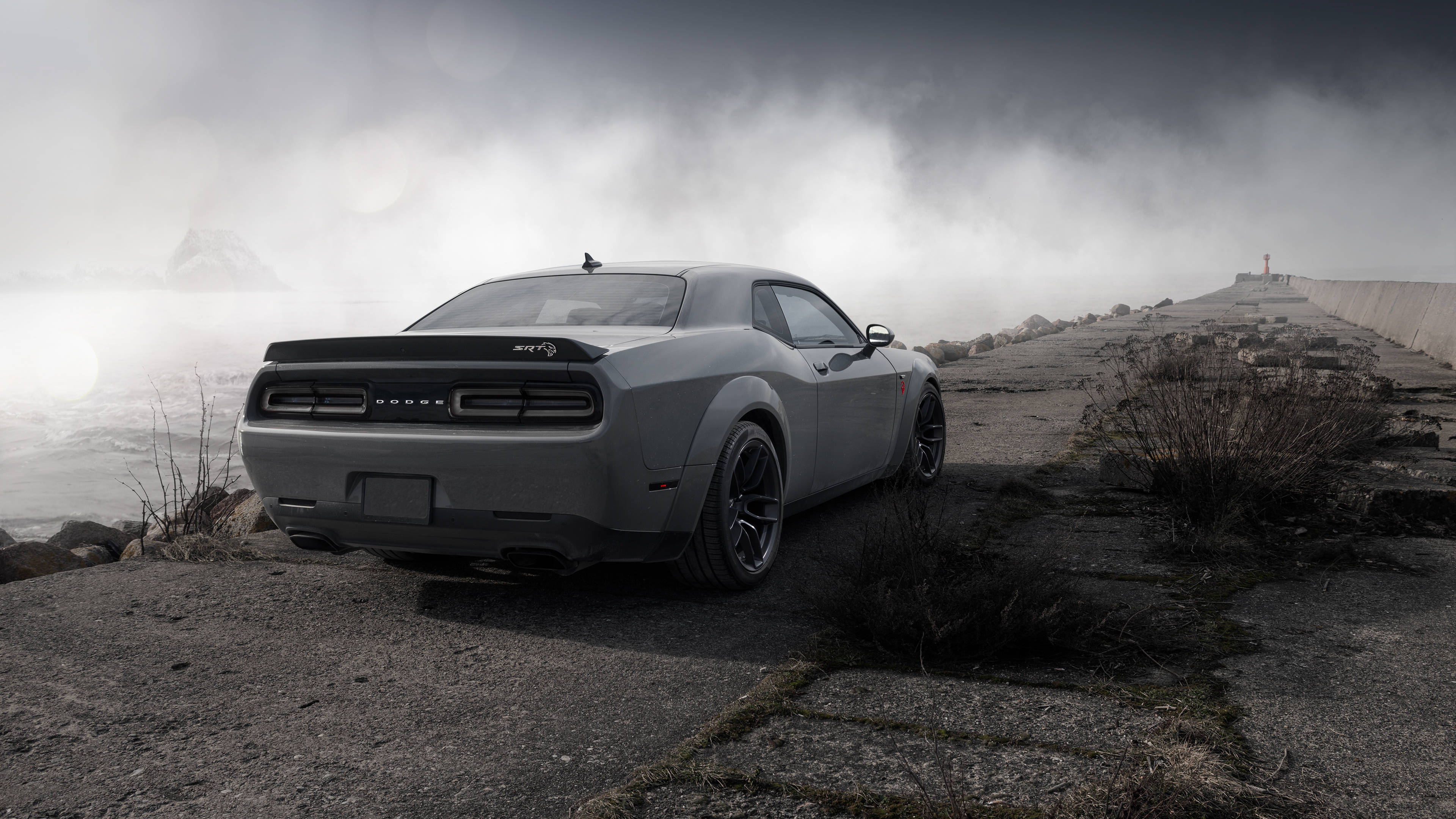 道奇挑戰者 桌布 壁紙 — 一架時尚的灰色 Dodge Challenger 停泊在霧氣瀰漫的懸崖上，俯瞰著波濤洶湧的大海和遠處的燈塔。