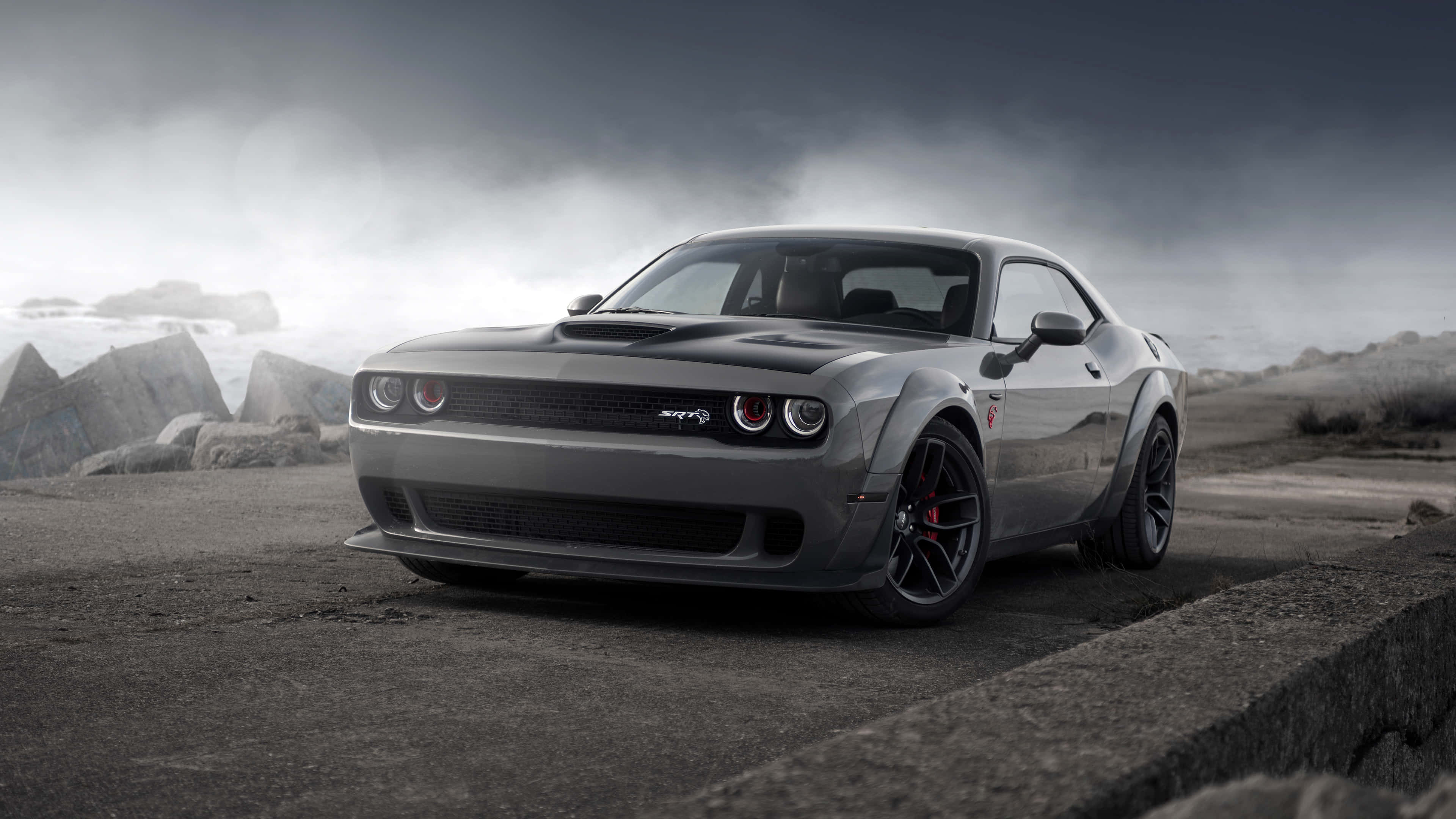 桌布 壁紙 — 一架時尚的灰色 Dodge Challenger SRT Hellcat 停放在混凝土邊緣上，背景是暴風雨的天空和參差不齊的岩石。