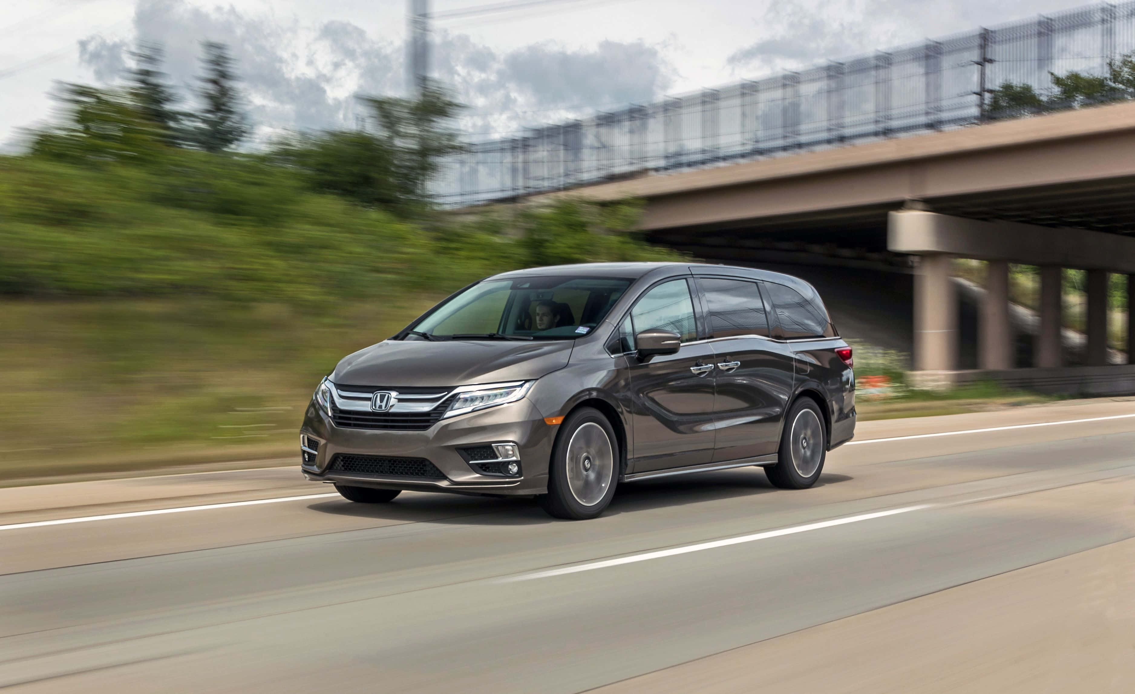 Honda Odyssey 桌布 壁紙 — 一架時尚的灰色小型貨車在混凝土高架橋下疾馳，伴隨著模糊的綠意和流動的天空。