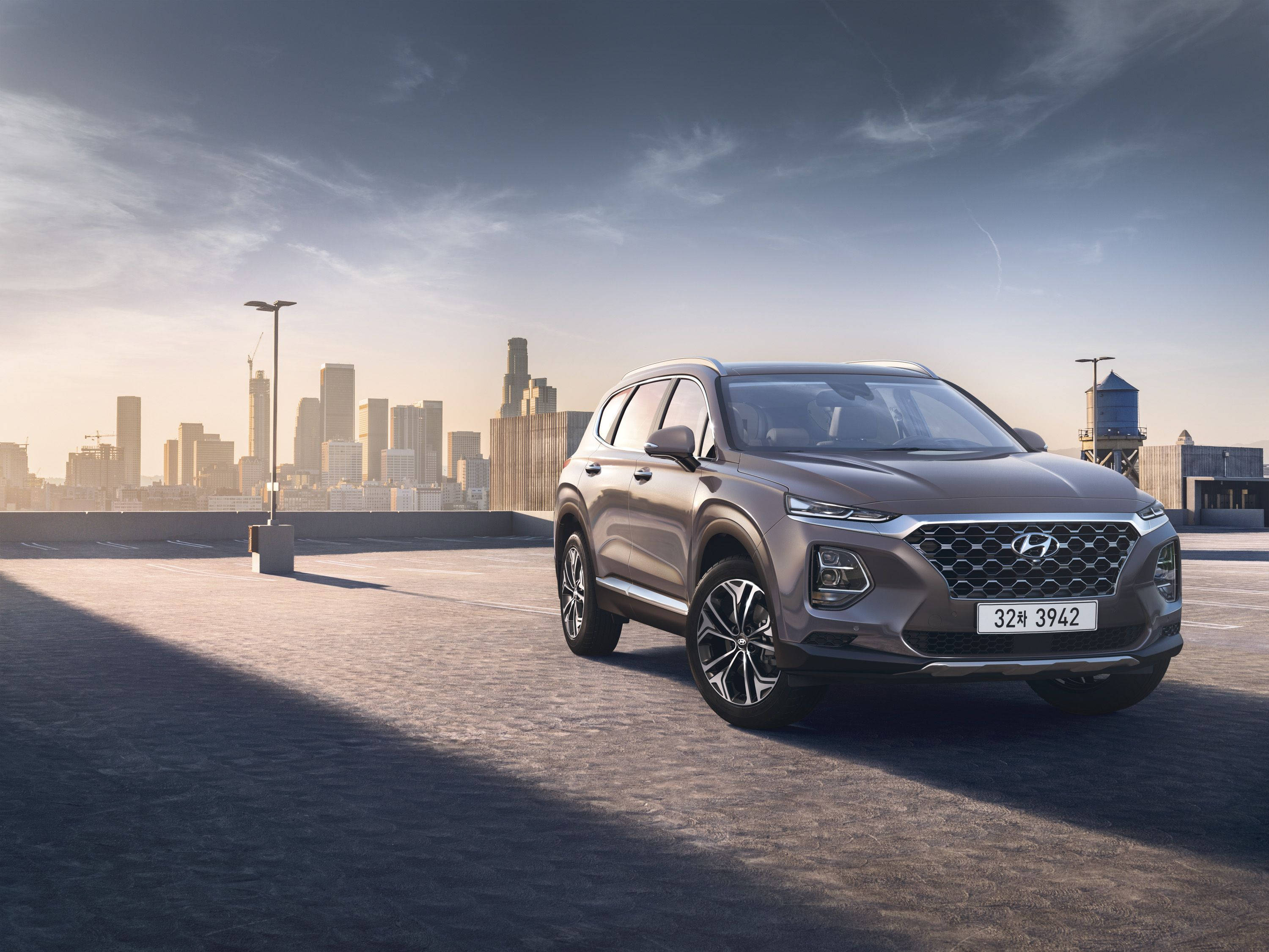 Hyundai 桌布 壁紙 — 一架時尚的灰色現代Santa Fe SUV停泊在屋頂上，現代城市天際線在黃金時段的光芒中閃耀。