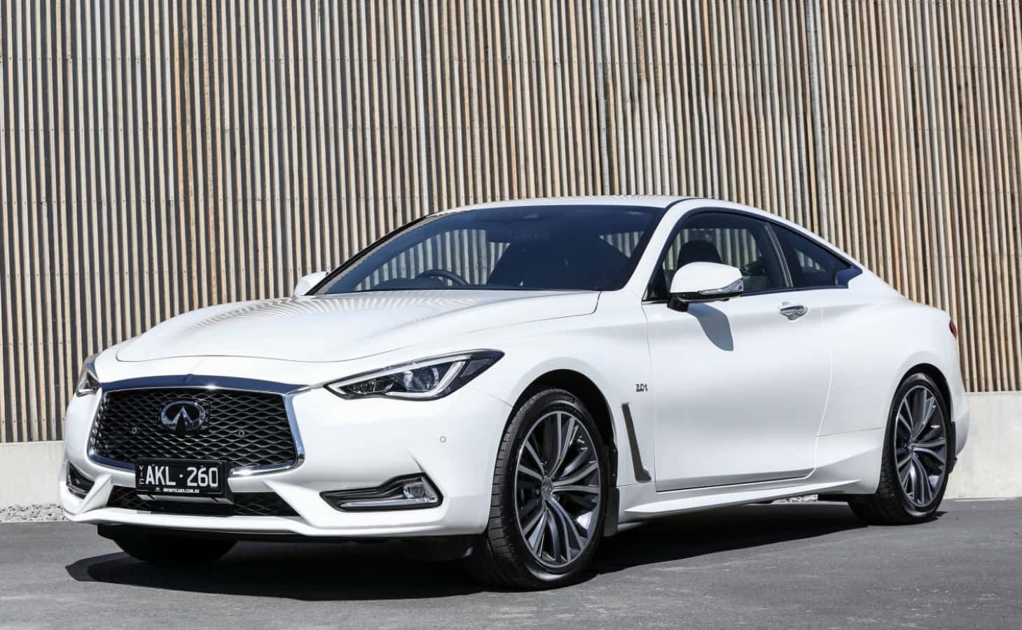 Infiniti Q60 桌布 壁紙 — 一架時尚的白色 Infiniti Q60 運動轎跑車停放在現代木條牆前，在明亮的日光下。