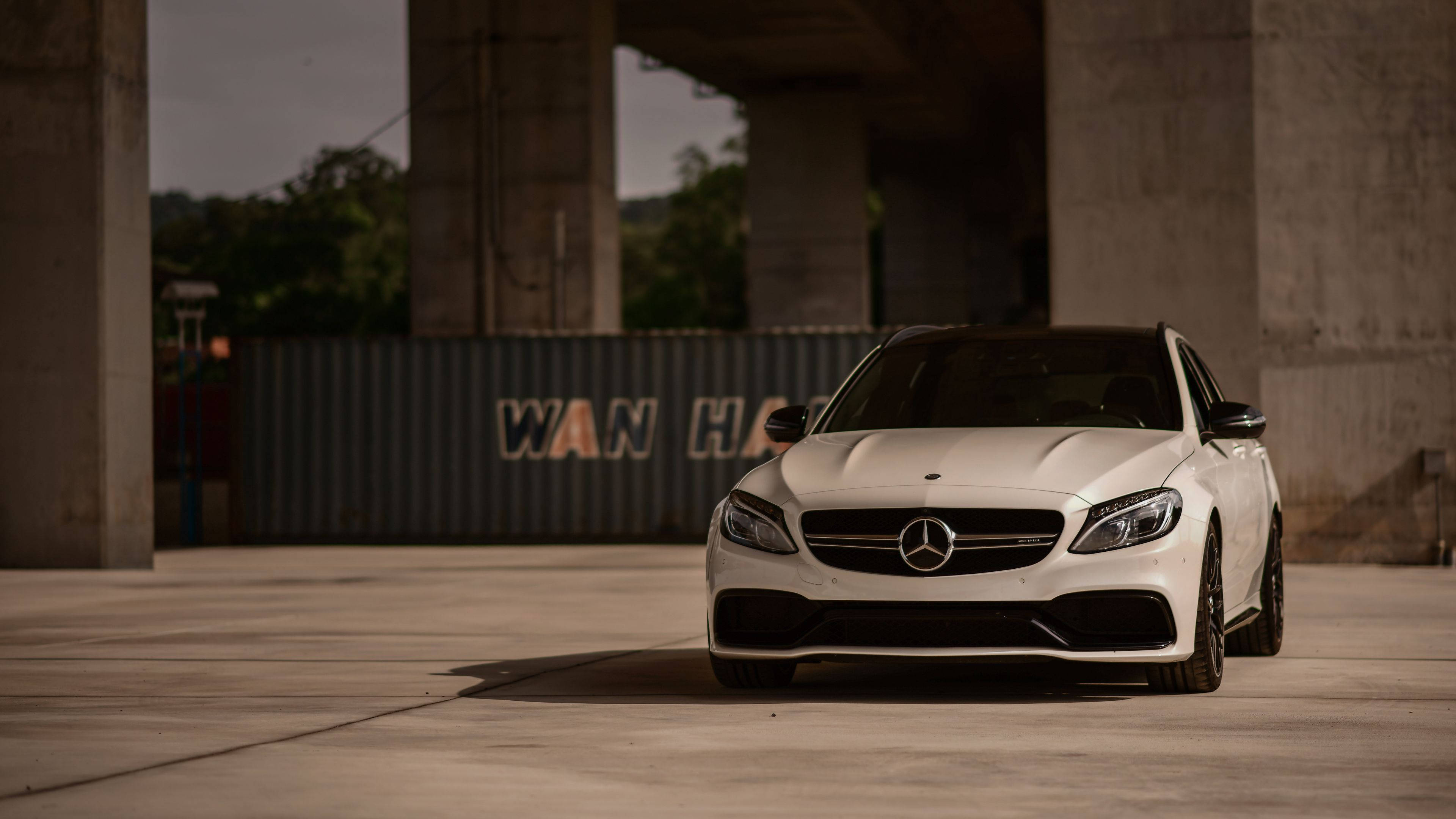 4K 奔馳壁紙 桌布 壁紙 — 一架時尚的白色 Mercedes-AMG C63 停放在混凝土高架橋下，背景有工業貨櫃。