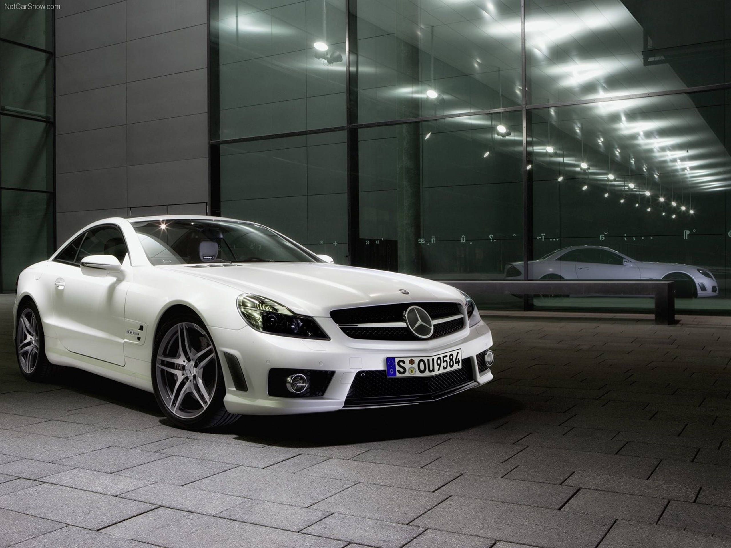 高清 桌布 壁紙 — 一架時尚的白色 Mercedes SLR McLaren 跑車在人造燈光下閃閃發光，停泊在現代玻璃建築旁邊的瓷磚廣場上。