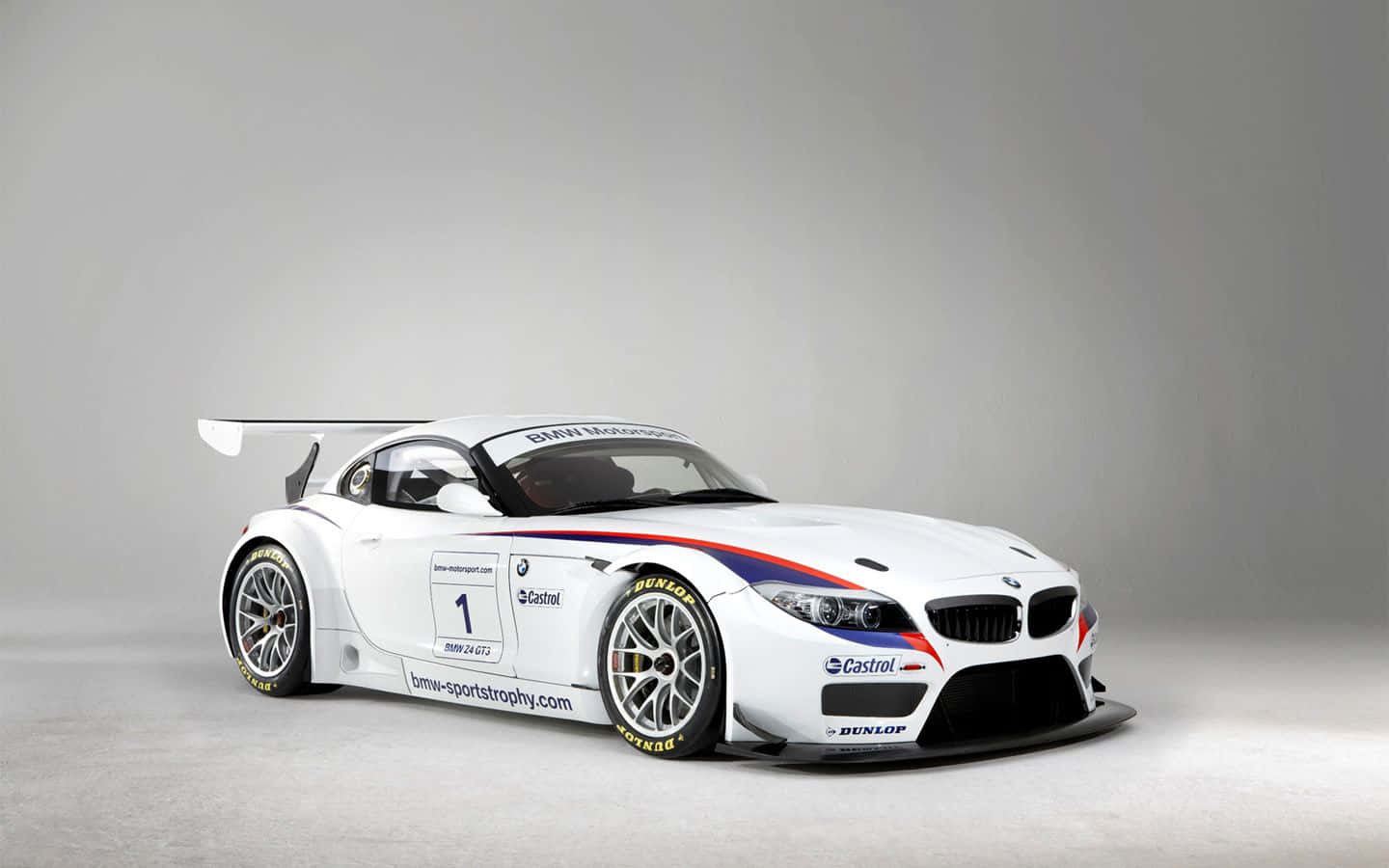 Bmw Z4 桌布 壁紙 — 一架時尚的白色BMW Z4賽車，帶有紅藍條紋和贊助商標誌，在極簡灰色工作室背景前擺拍。