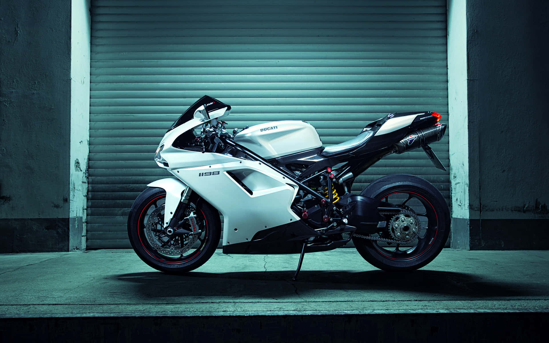 Superbike 桌布 壁紙 — 一架時尚的白色Ducati 998機車，在清涼的人造燈光下，停放在青綠色金屬車庫門前。