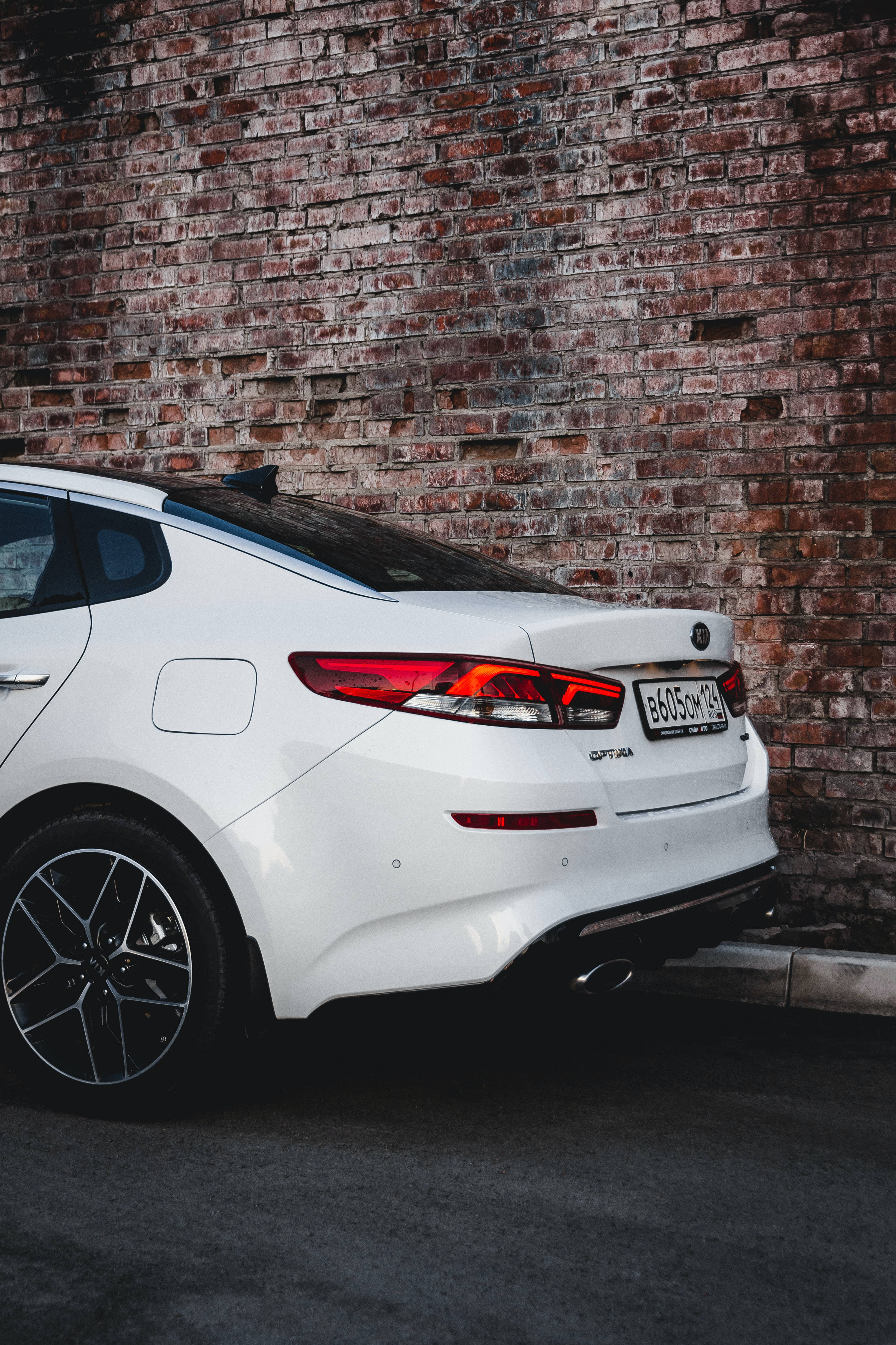 Kia 桌布 壁紙 — 一架時尚的白色Kia Stinger停泊在風化磚牆旁，帶有戲劇性的燈光。