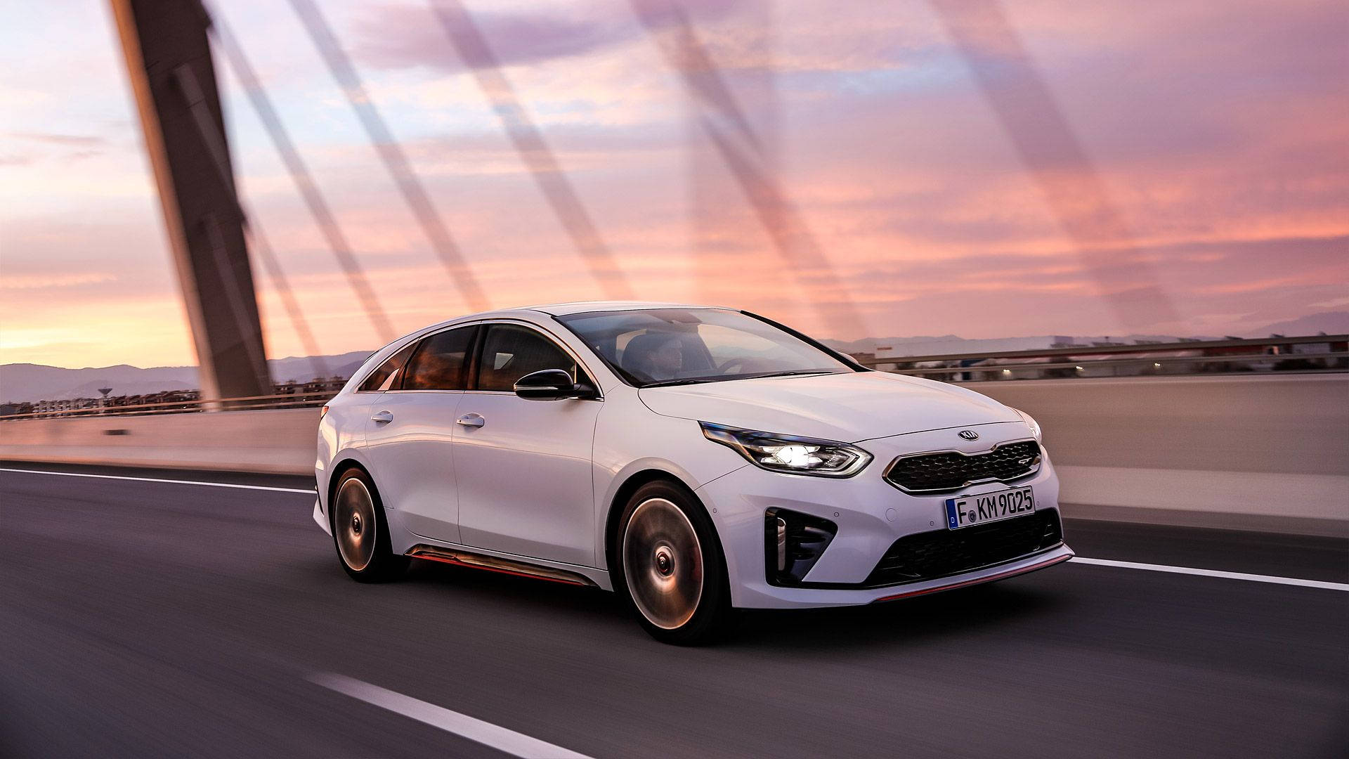 Kia 桌布 壁紙 — 一架時尚的白色Kia轎車在充滿活力的粉紅色和橙色日落天空下，飛馳過一座現代橋樑。