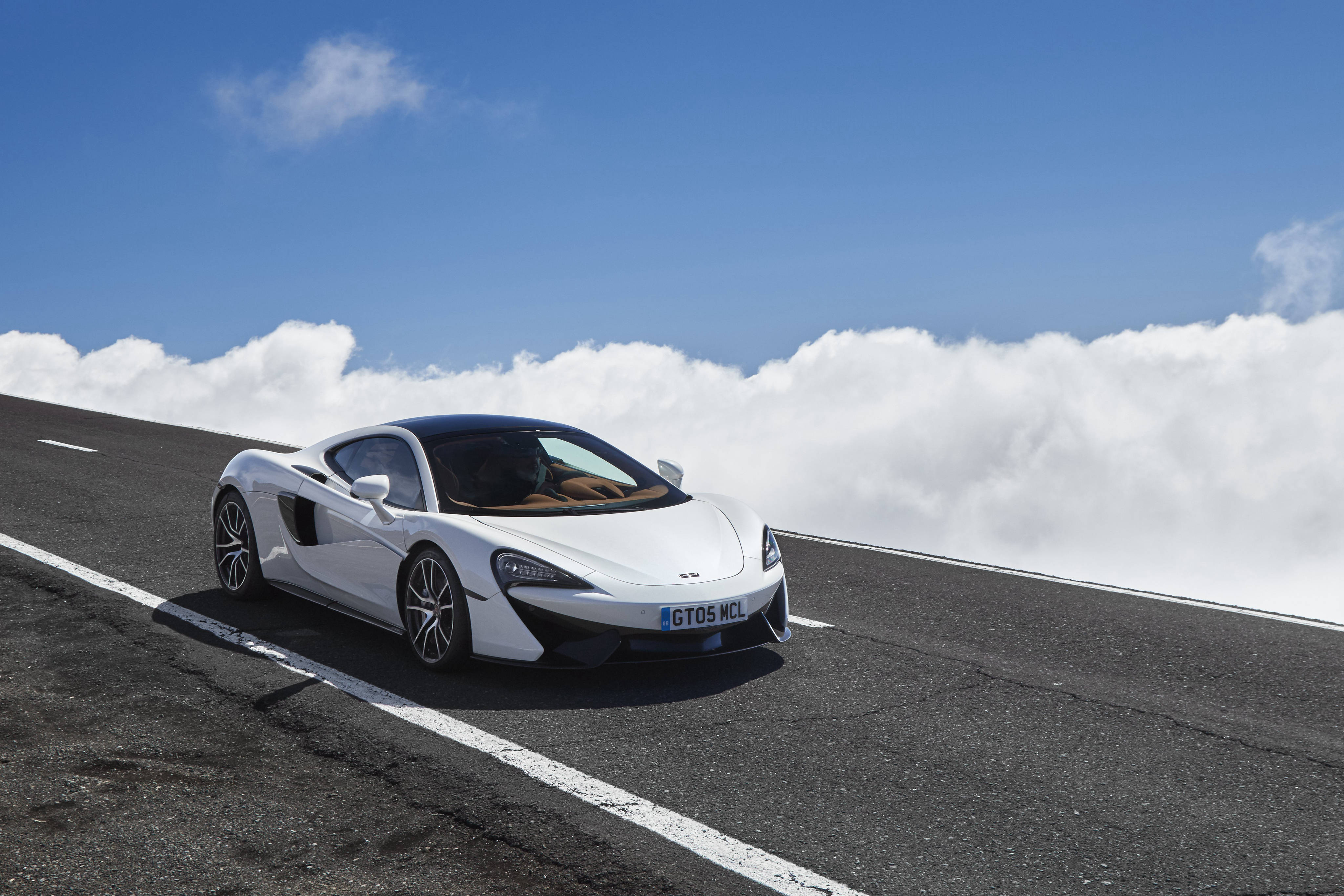 麥拉倫 桌布 壁紙 — 一架時尚的白色McLaren跑車在晴朗藍天下，行駛在雲海之上的高山公路上。