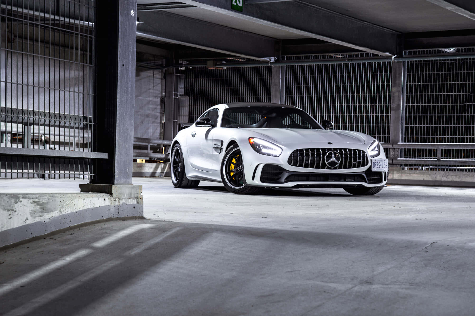 汽車 桌布 壁紙 — 一架時尚的白色Mercedes-AMG GT停放在混凝土地下停車場，配有工業金屬圍欄和戲劇性燈光。