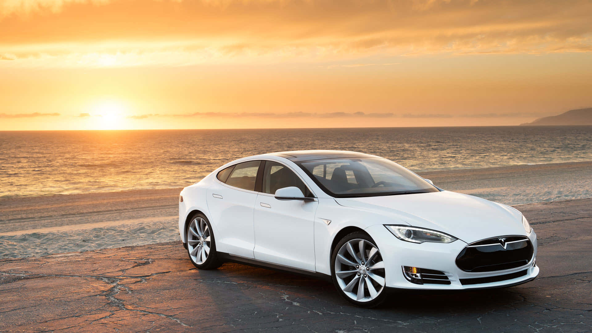 特斯拉 桌布 壁紙 — 一架時尚的白色Tesla Model S停泊在龜裂的瀝青海灘上，金色夕陽與海浪翻滾。